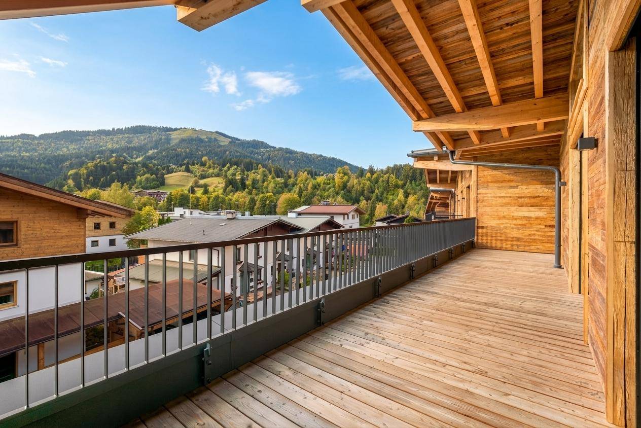 Langer Holzbalkon mit Metallgeländer und Blick auf die grünen Hügel und Nachbargebäude.