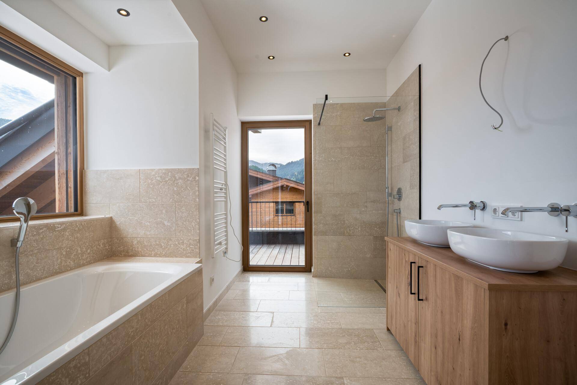 Modernes Badezimmer mit Badewanne, begehbarer Dusche, Doppelwaschbecken und Zugang zum Außenbereich.