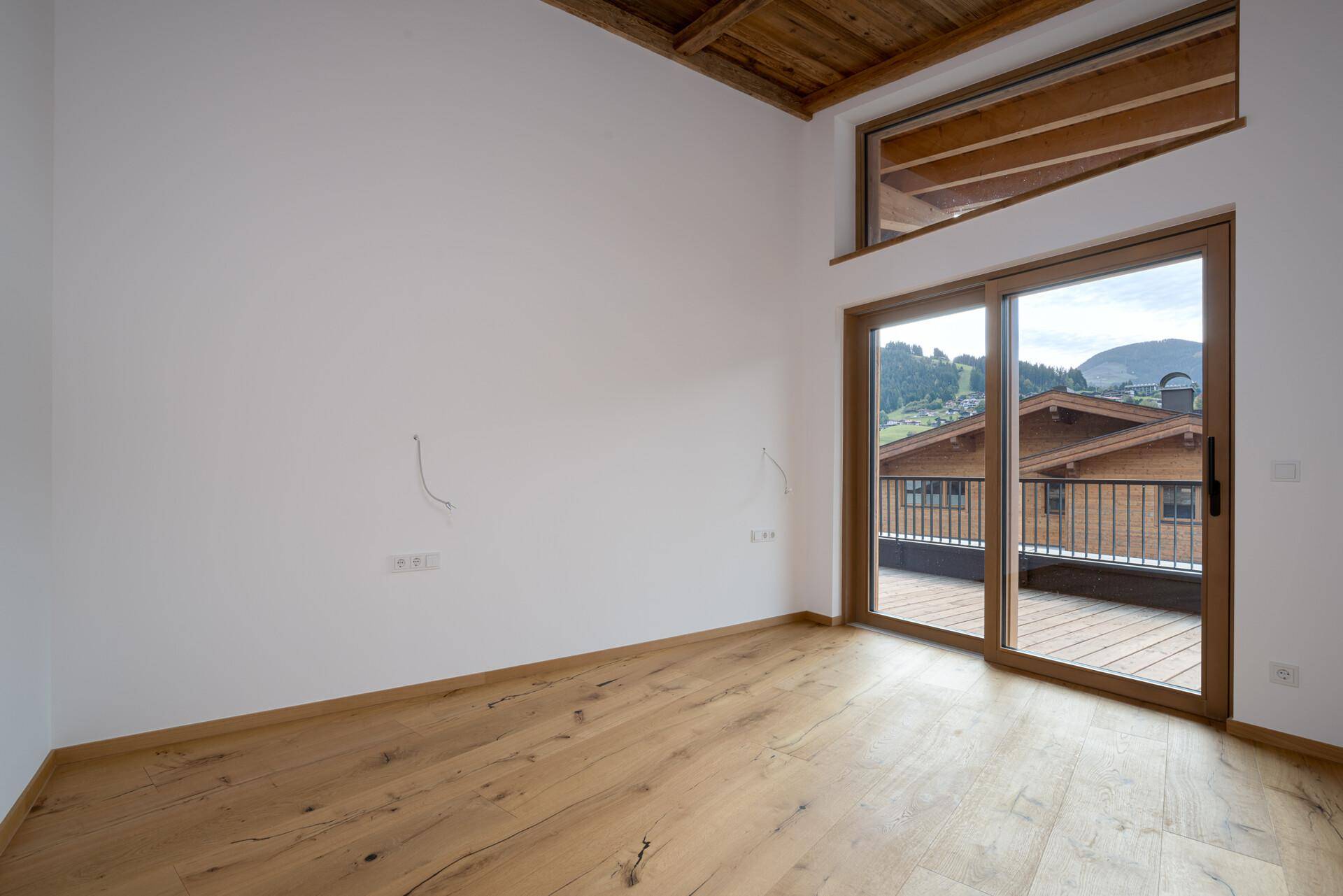 Geräumiges, leeres Zimmer mit Holzboden, Holzbalkendecke und Schiebetür zur Terrasse.