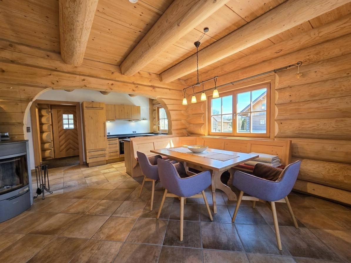Gemütlicher Essbereich in einem Blockhaus mit Holzbalken, Fliesenboden und Kaminofen.