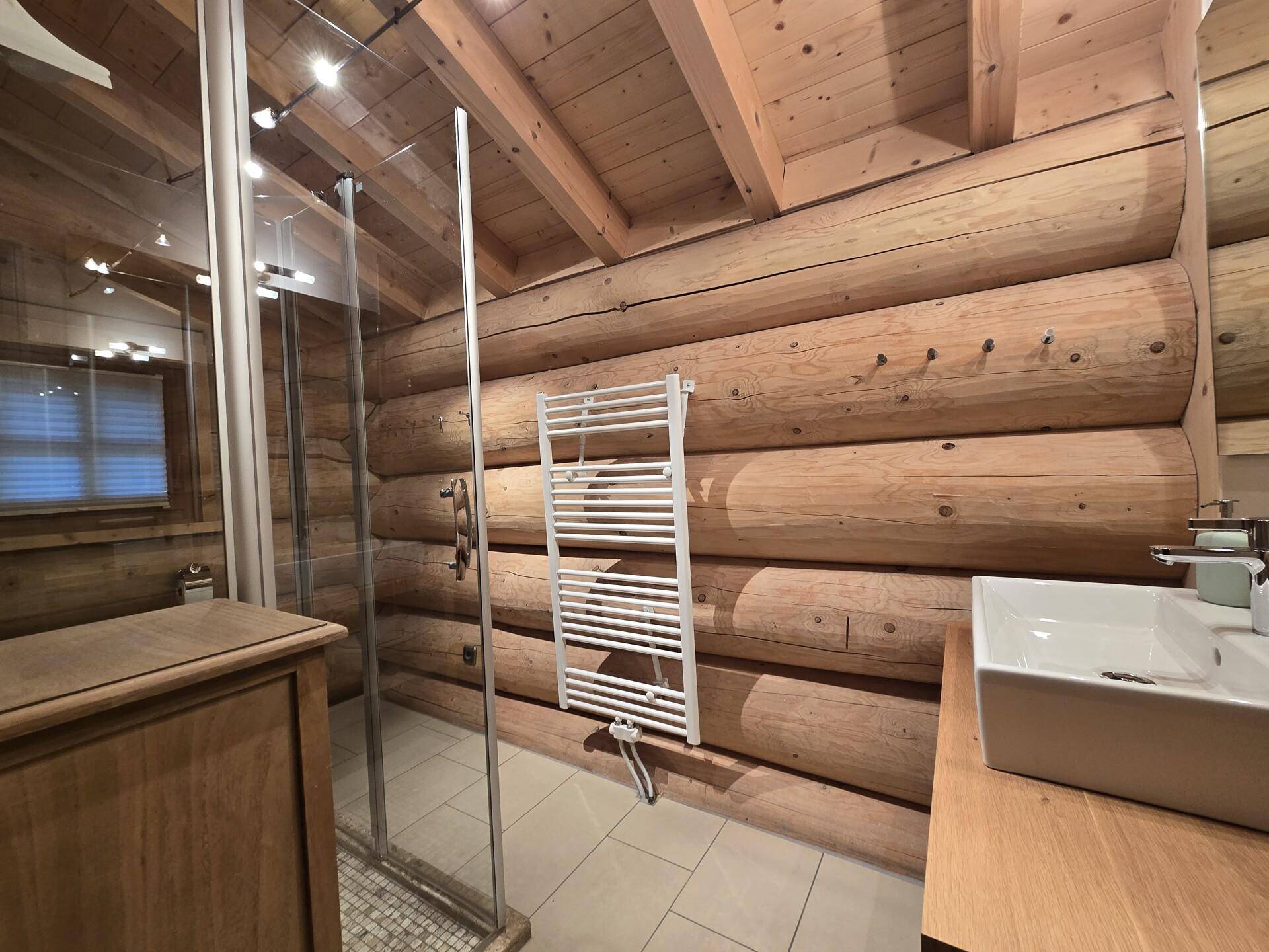 Badezimmer mit Dusche, beheiztem Handtuchhalter und Holzwänden im Blockhausstil.