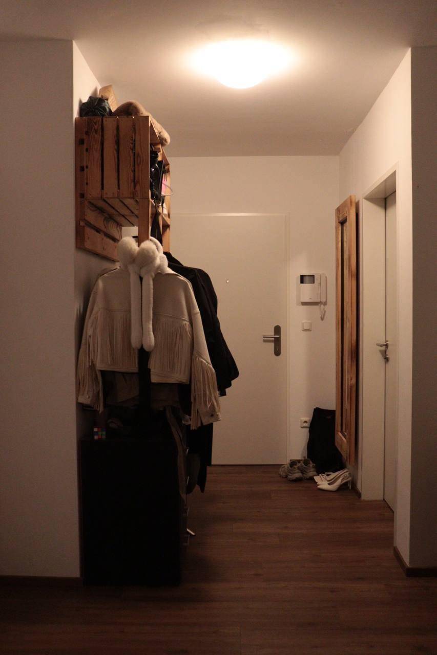 Heller Flur mit Garderobe, Holzkisten als Ablage und einer weißen Eingangstür.