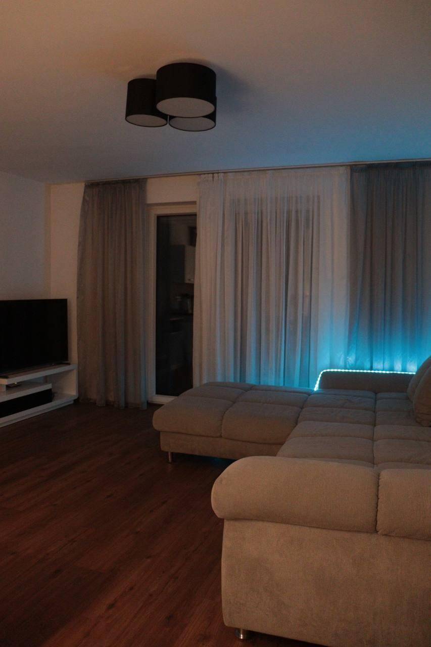 Gemütliches Wohnzimmer am Abend mit Sofa, Fernseher und stimmungsvoller blauer Beleuchtung.