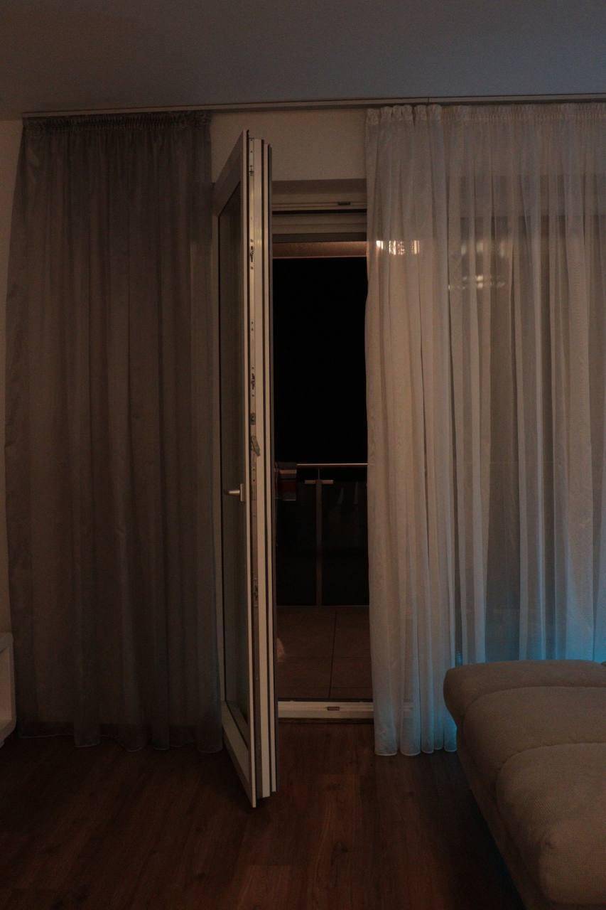 Offene Balkontür in einem Wohnzimmer bei Nacht, die den Zugang zum Außenbereich ermöglicht.