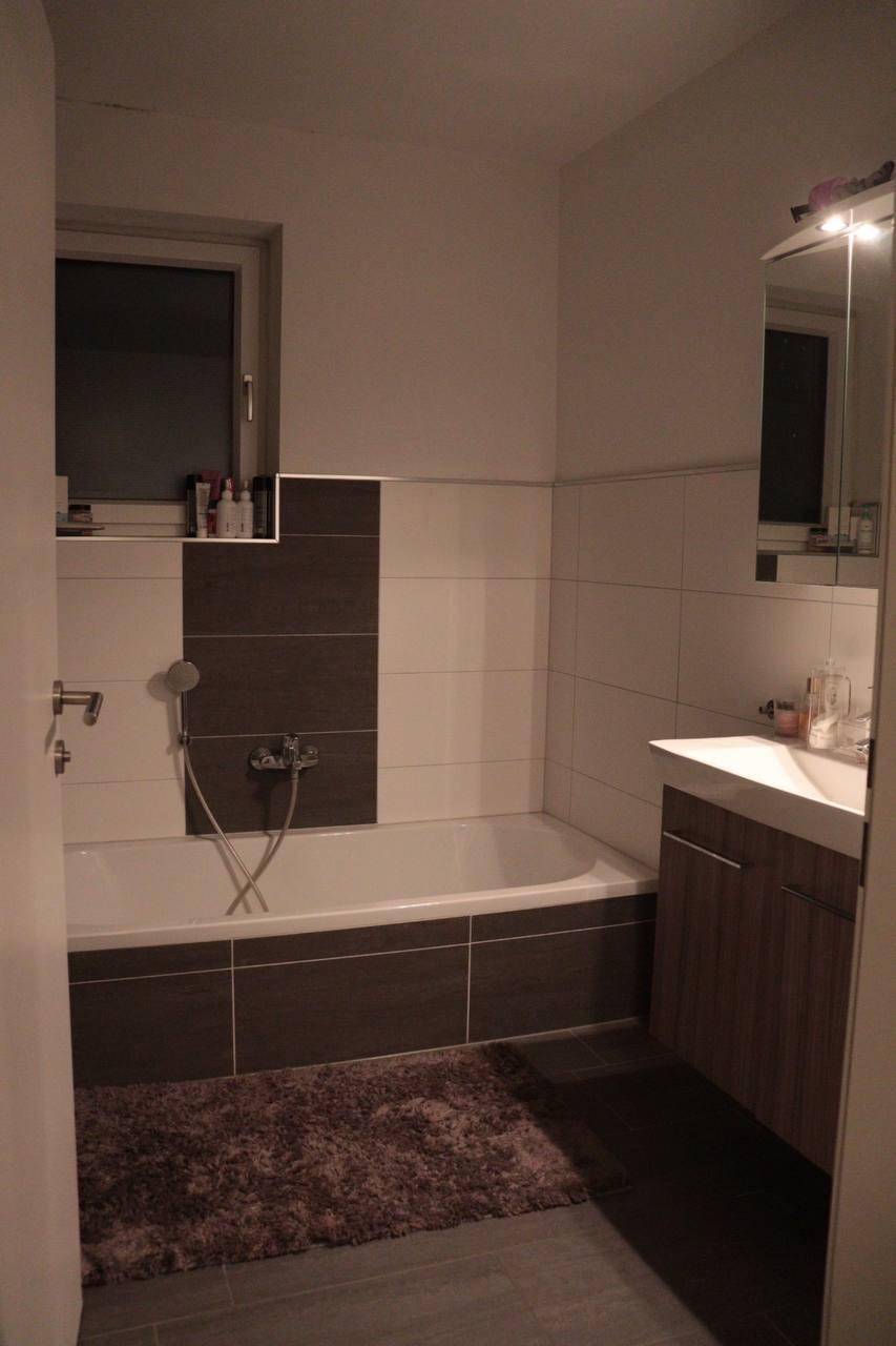 Badezimmer mit Badewanne, Waschtischunterschrank und Spiegelschrank, in modernen Fliesen gehalten.