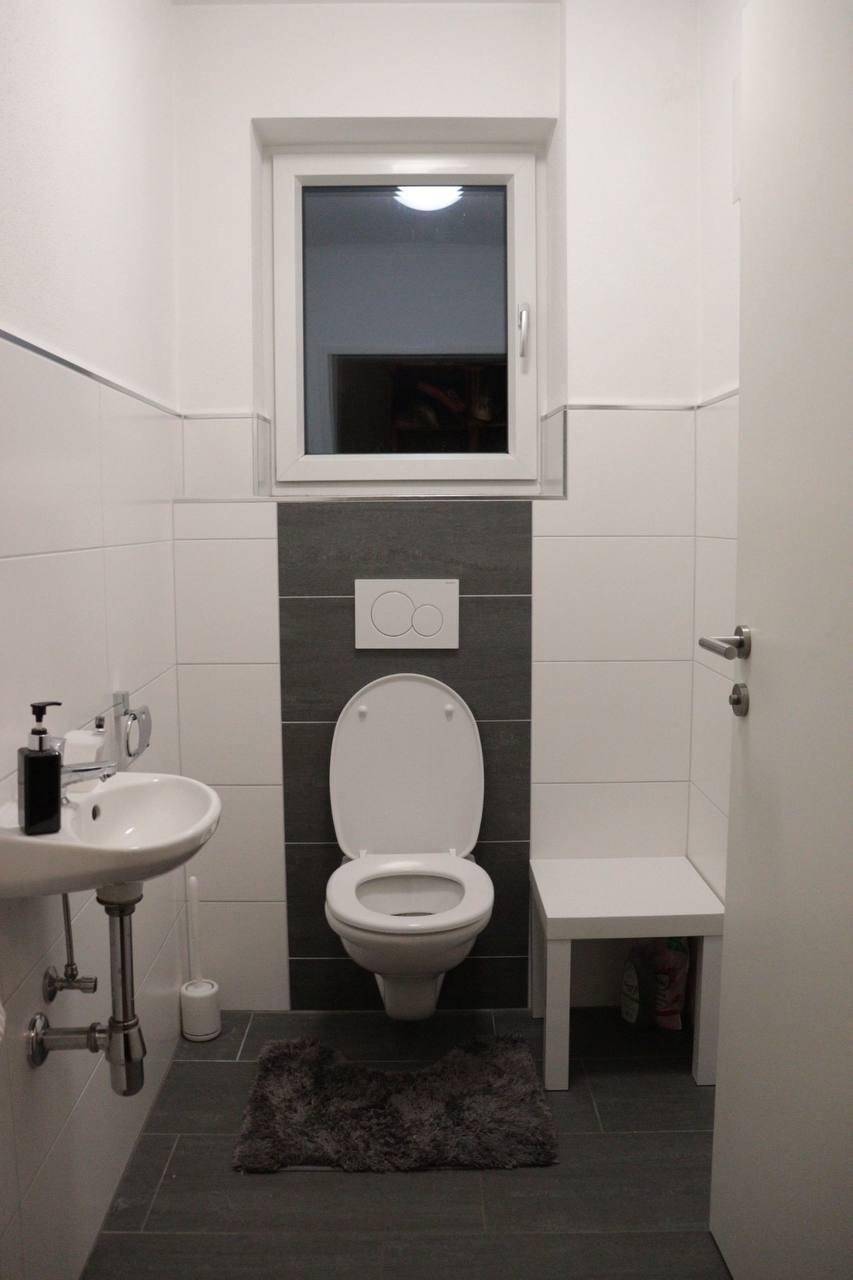 Modernes Gäste-WC mit wandhängender Toilette, kleinem Waschbecken und einem Fenster für Tageslicht.