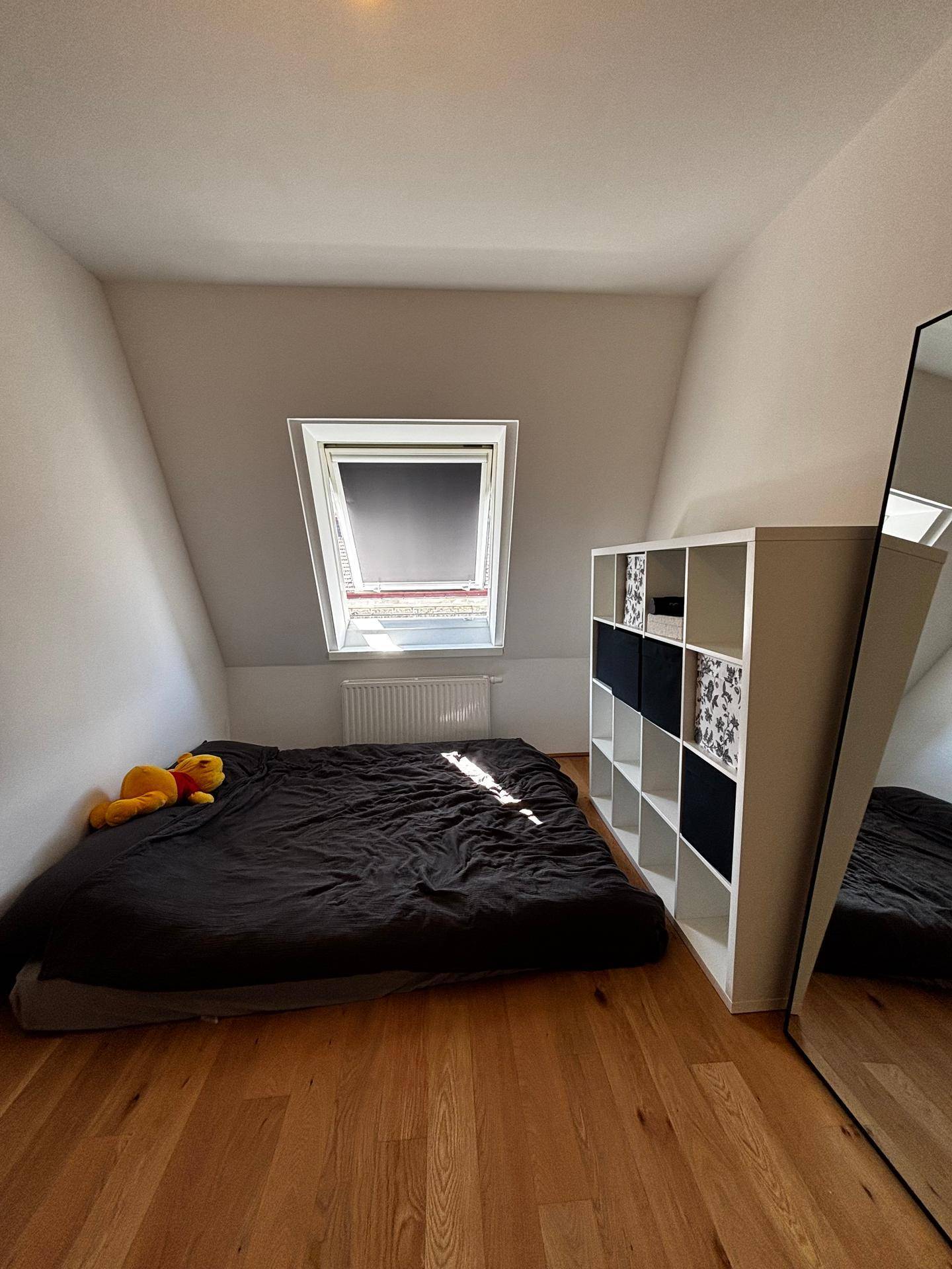 Helles Schlafzimmer mit Holzboden, Dachfenster, niedrigem Bett und praktischem Regal.