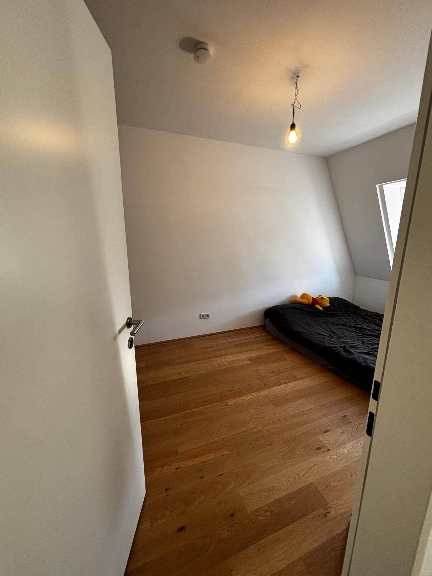 Schlafzimmer im Dachgeschoss mit Holzboden, Dachfenster und einfacher Bettausstattung.