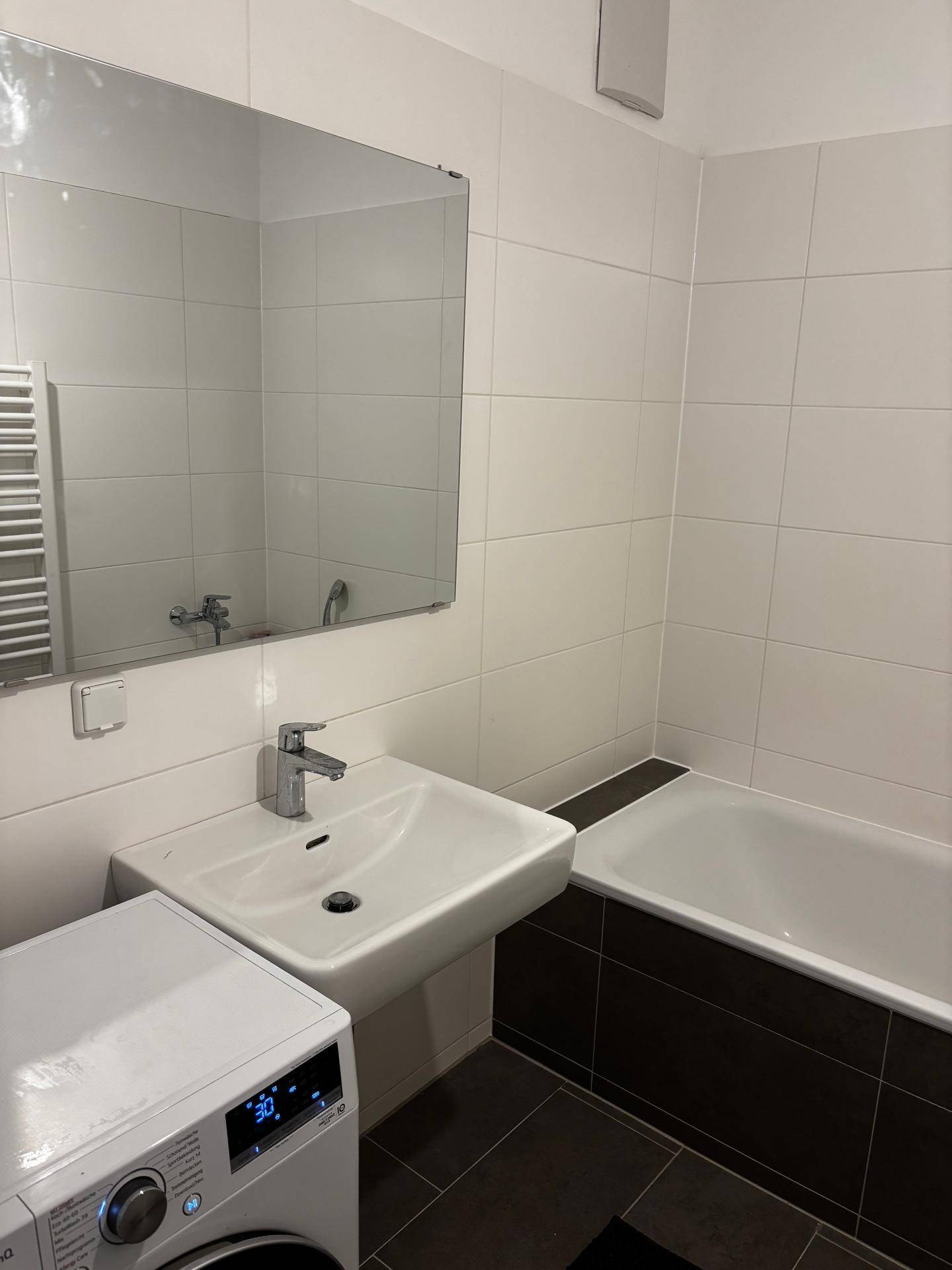 Modernes Badezimmer mit weißem Waschbecken, Badewanne und großem Wandspiegel.