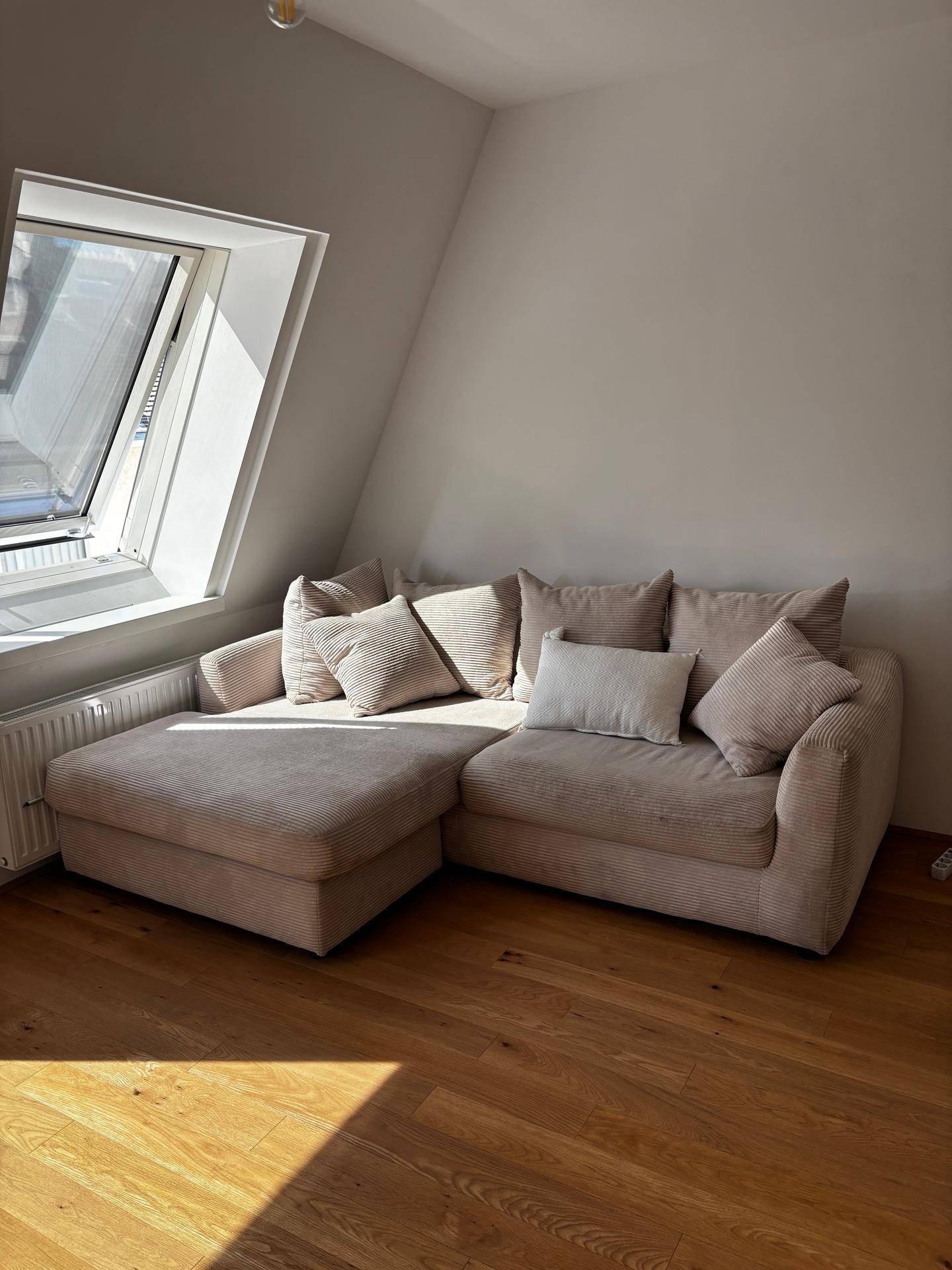 Gemütliches Sofa im hellen Wohnzimmer mit Holzboden und viel Tageslicht durch Dachfenster.