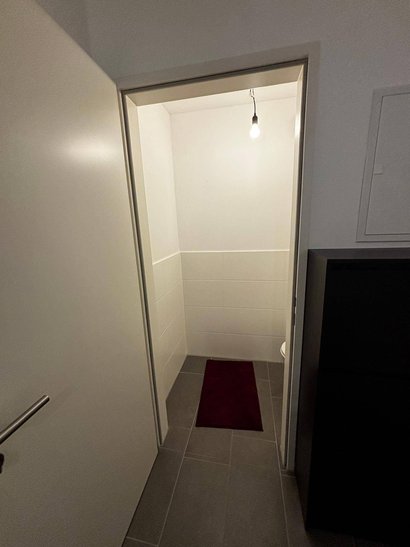 Blick in ein kleines Gäste-WC mit weißen Fliesen und dunklem Boden.