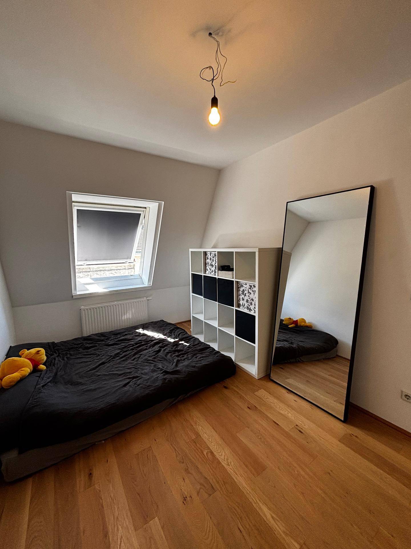 Schlafzimmer im Dachgeschoss mit Holzboden, Dachfenster, Regal und großem Standspiegel.