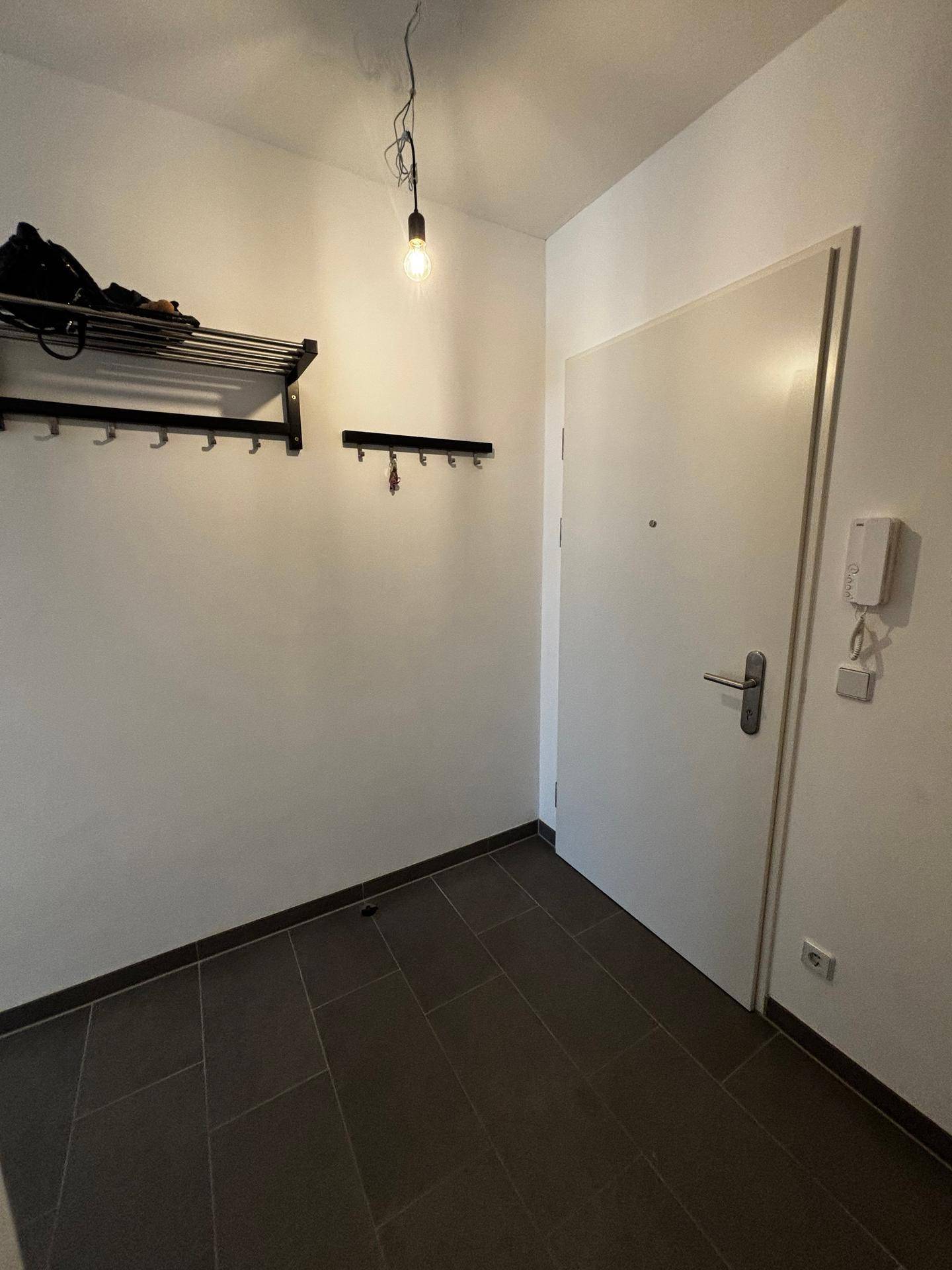Eingangsbereich mit dunklem Fliesenboden, Garderobe und Gegensprechanlage.