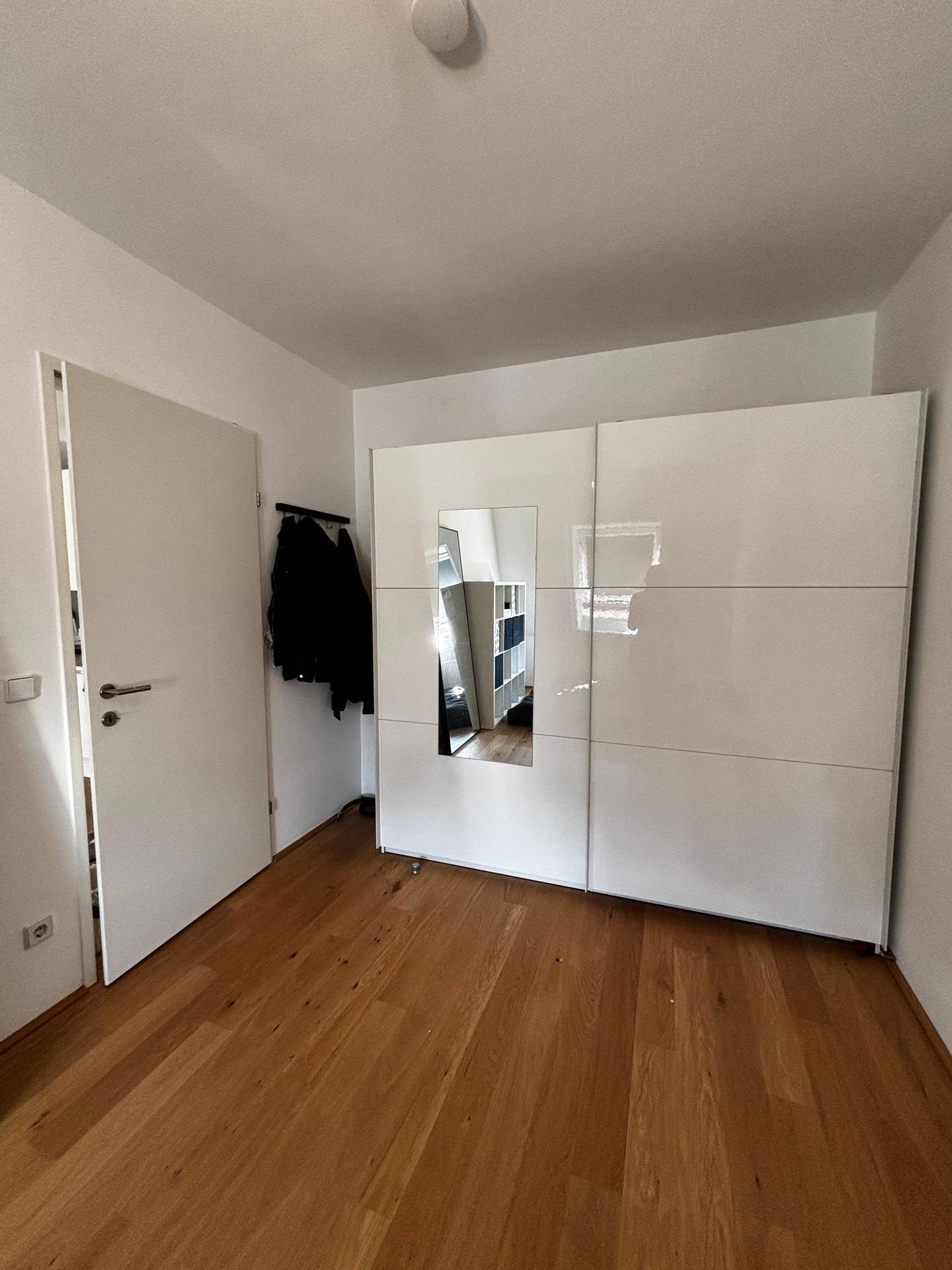 Schlafzimmer mit Holzboden und großem, weißem Kleiderschrank mit Spiegelfront.