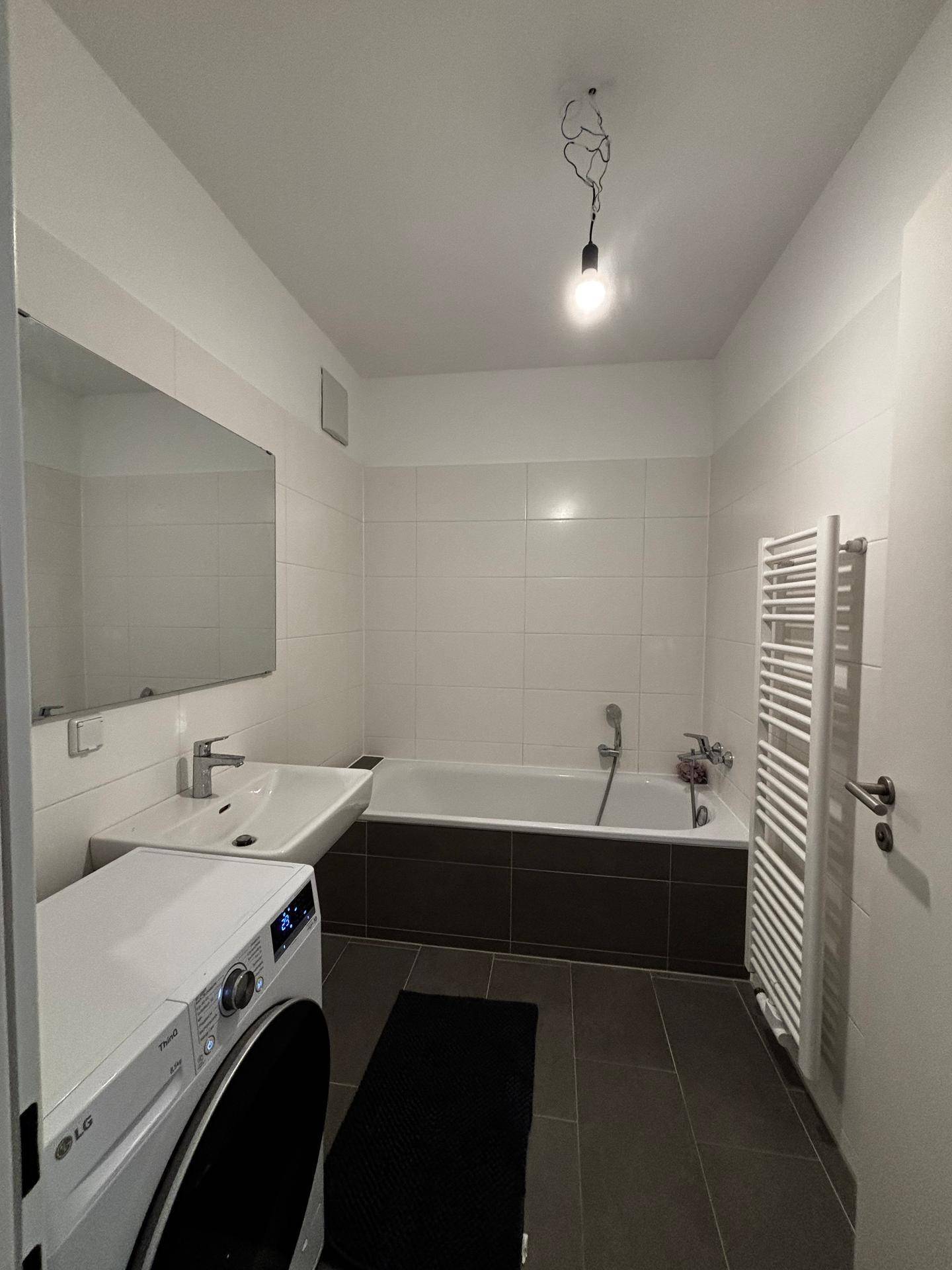 Funktionales Badezimmer mit Badewanne, Waschbecken, Spiegel und praktischem Handtuchheizkörper.