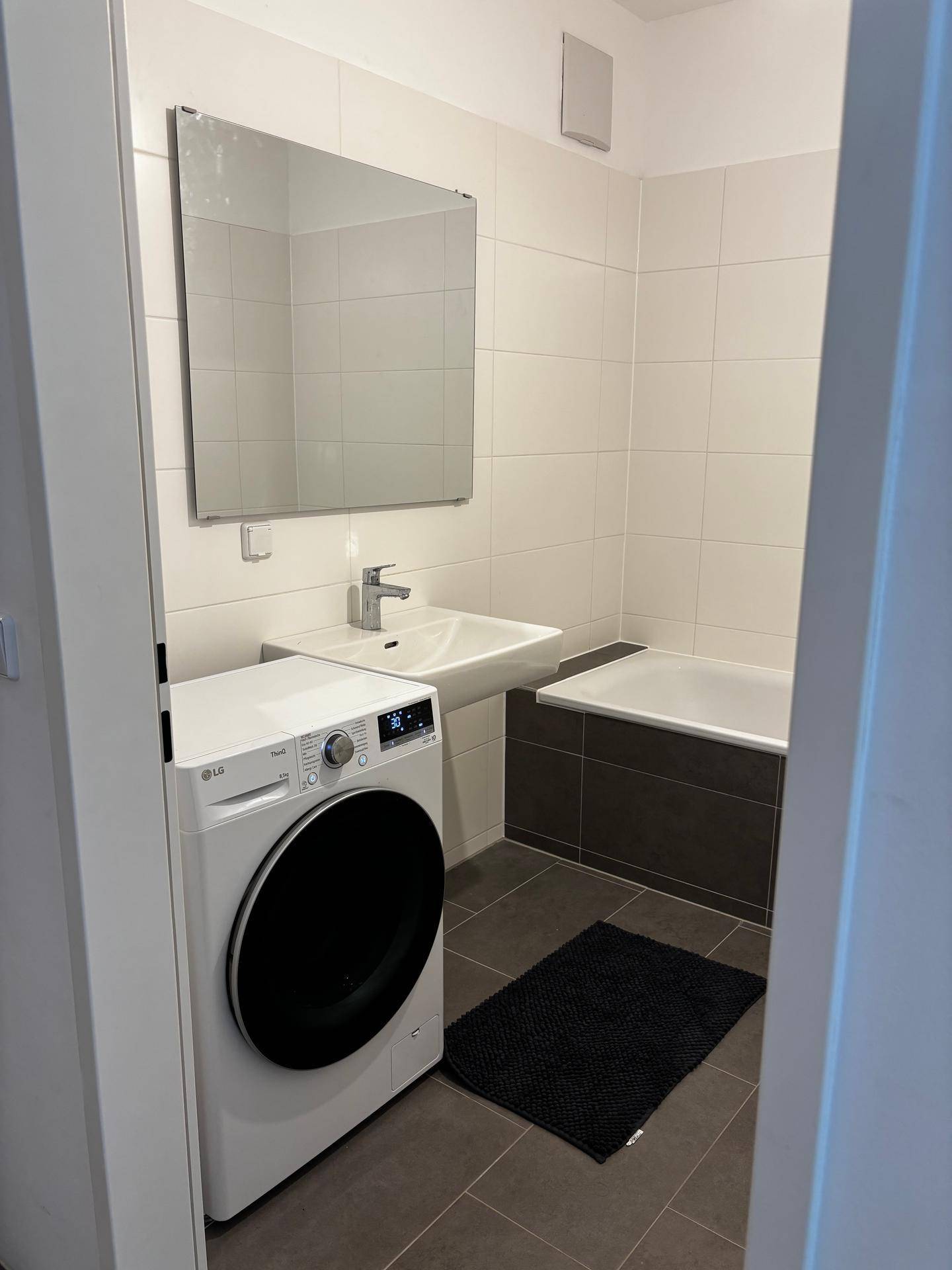 Badezimmer mit Badewanne, Waschbecken und integrierter Waschmaschine.