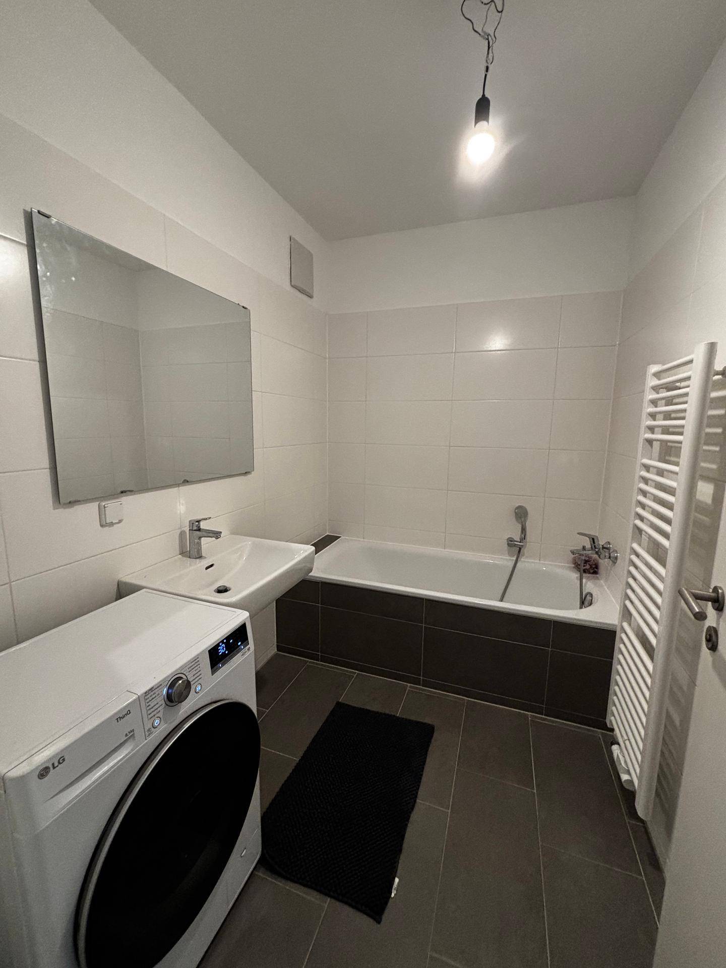 Helles Badezimmer mit Badewanne, Waschbecken, Spiegel und Handtuchheizkörper.