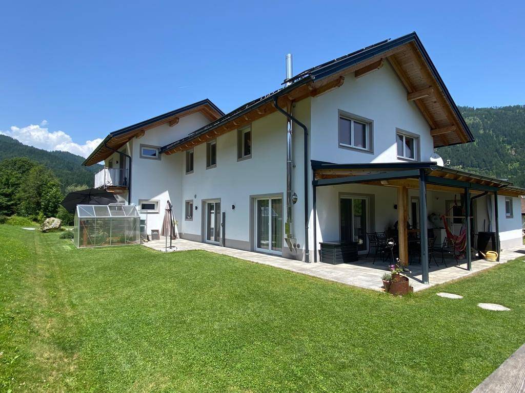 Modernes Einfamilienhaus mit großem Garten, überdachter Terrasse und Bergblick.