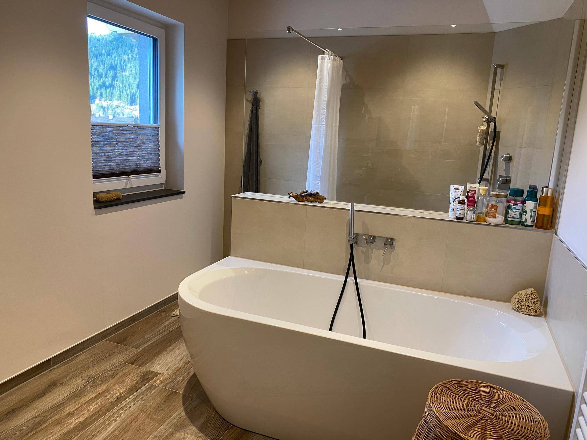 Modernes Badezimmer mit freistehender Badewanne, Dusche und Fenster mit Bergblick.