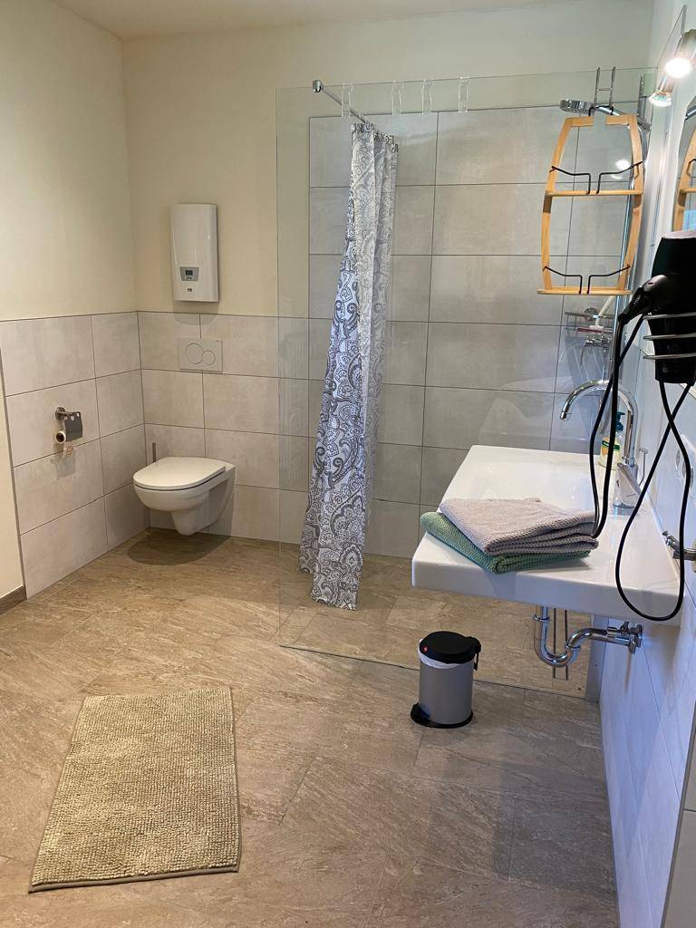 Helles Badezimmer mit Dusche, Toilette, Einzelwaschbecken und großformatigen Fliesen.