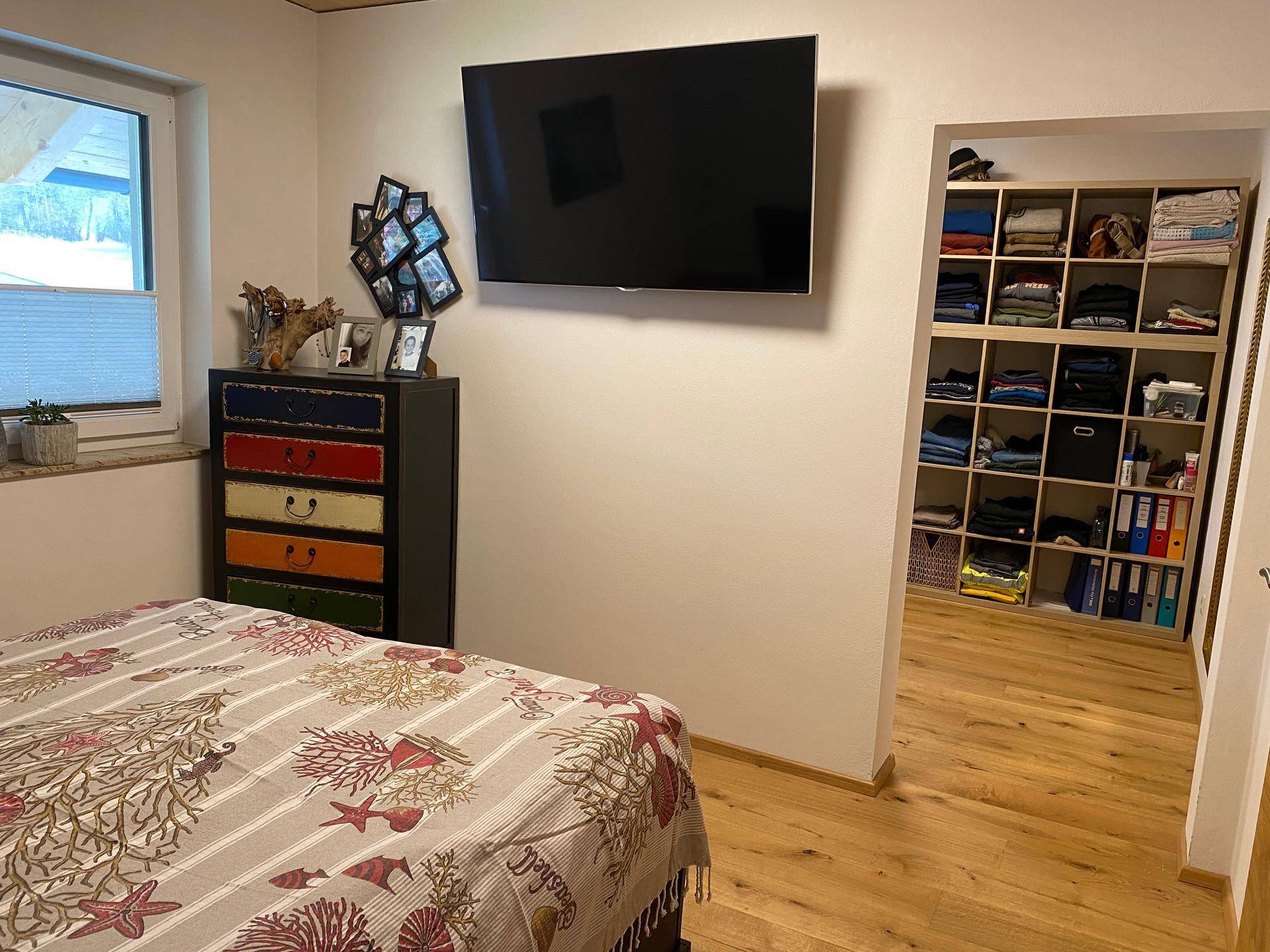 Schlafzimmer mit Doppelbett, Wandfernseher und offenem Zugang zu einem begehbaren Kleiderschrank.