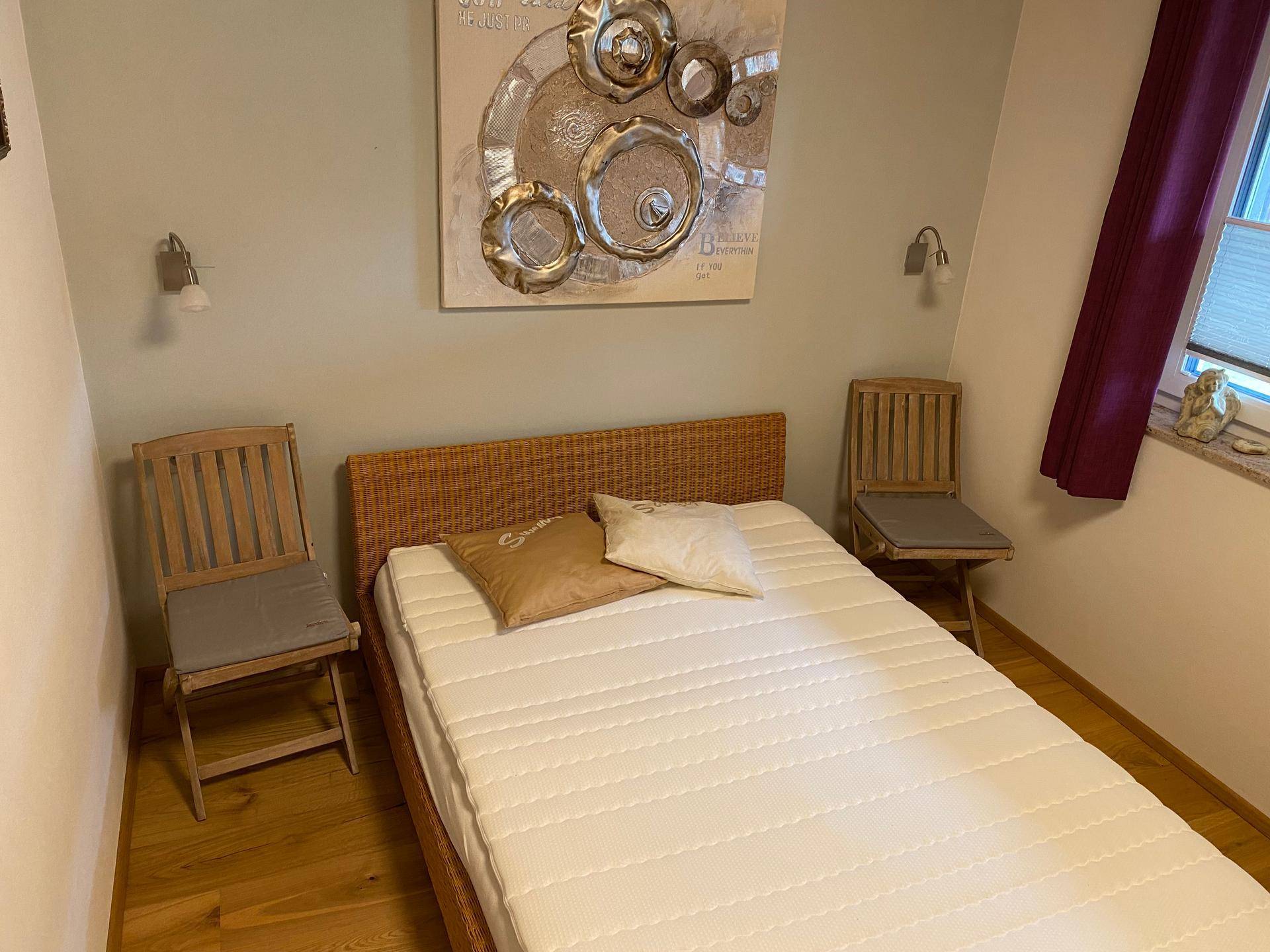 Schlafzimmer mit Rattanbett, Holzboden und dekorativer Wandkunst über dem Bett.