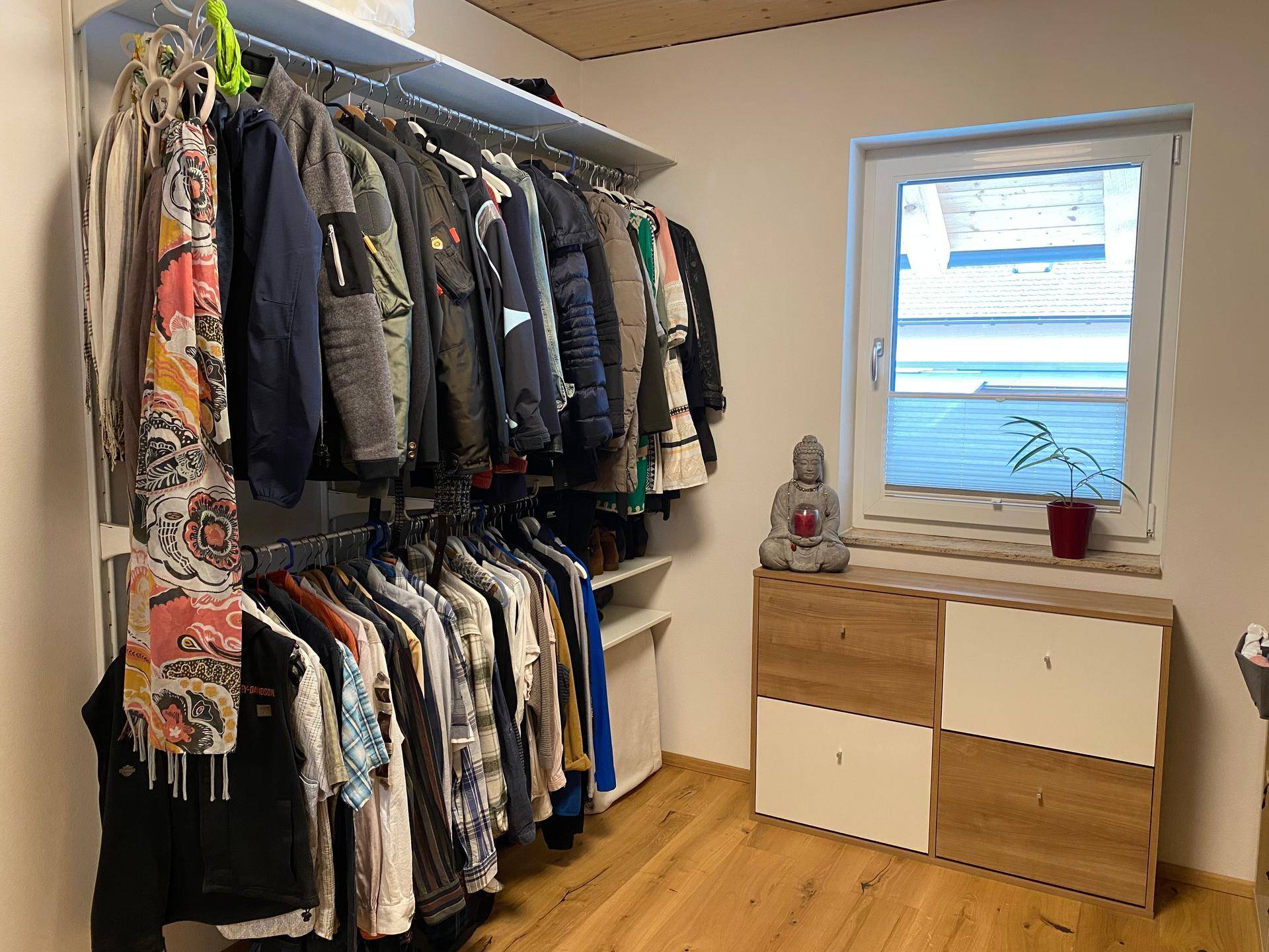 Praktischer begehbarer Kleiderschrank mit Kleiderstangen, Regalen und Fenster für natürliche Belichtung.