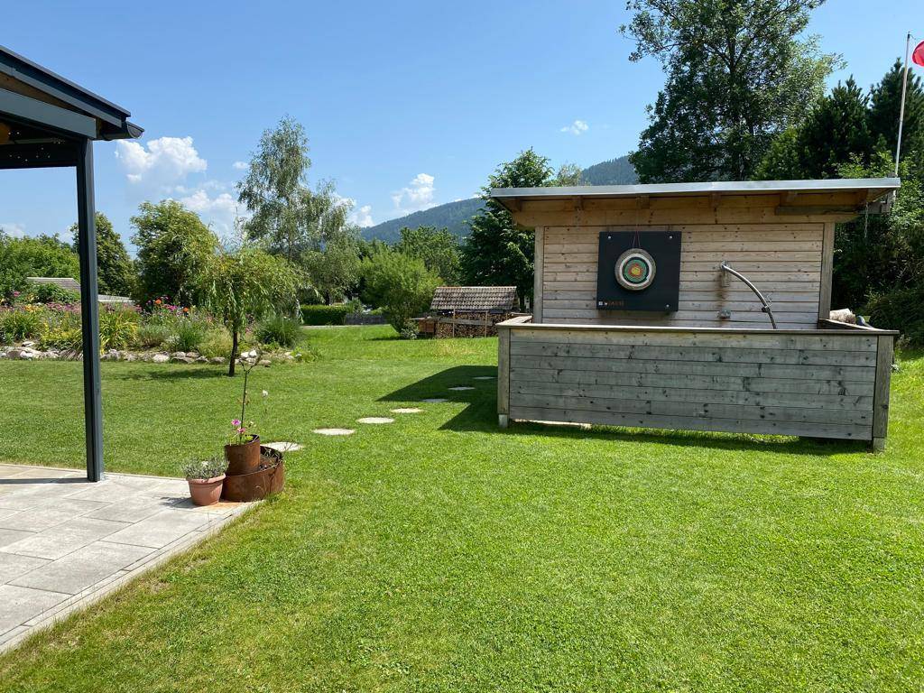 Großer grüner Gartenbereich mit Holzkonstruktion, Rasenfläche und gepflastertem Terrassenweg.