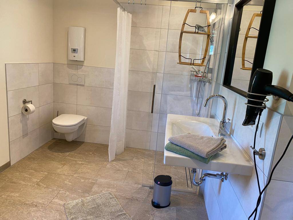 Helles Badezimmer mit Dusche, Toilette, Einzelwaschbecken und großformatigen Fliesen.