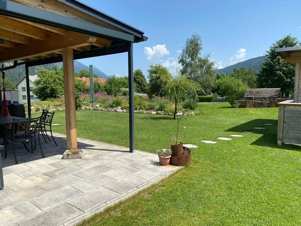 Überdachte Terrasse mit Esstisch und Stühlen, umgeben von einem weitläufigen Garten.