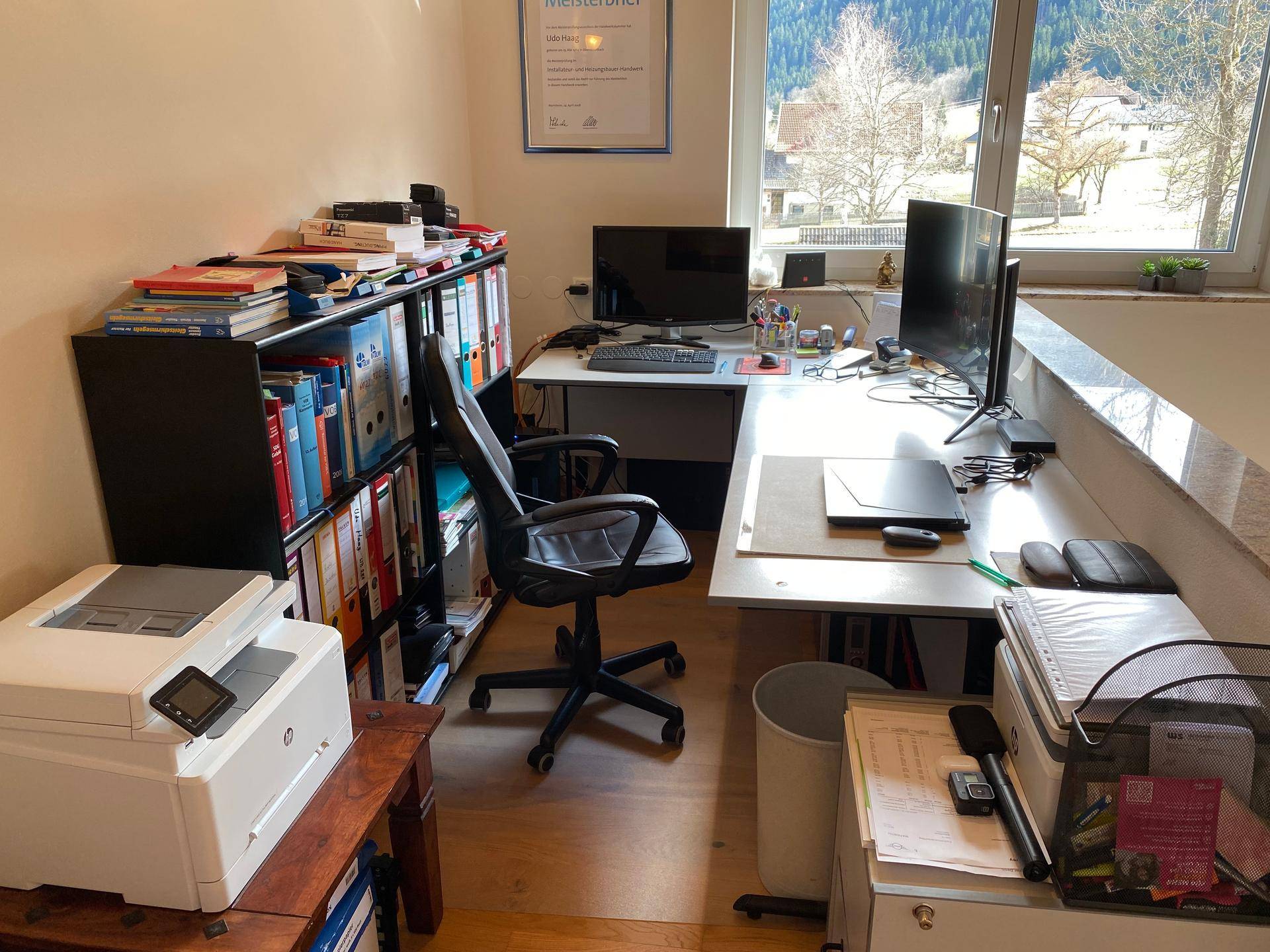 Helles Heimbüro mit Schreibtisch, Computern und Blick auf die umliegende Landschaft.