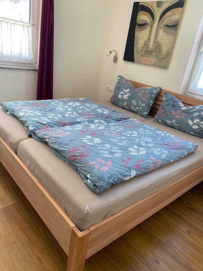 Schlafzimmer mit Doppelbett, Holzboden und farbenfroher Bettwäsche unter natürlichem Licht.