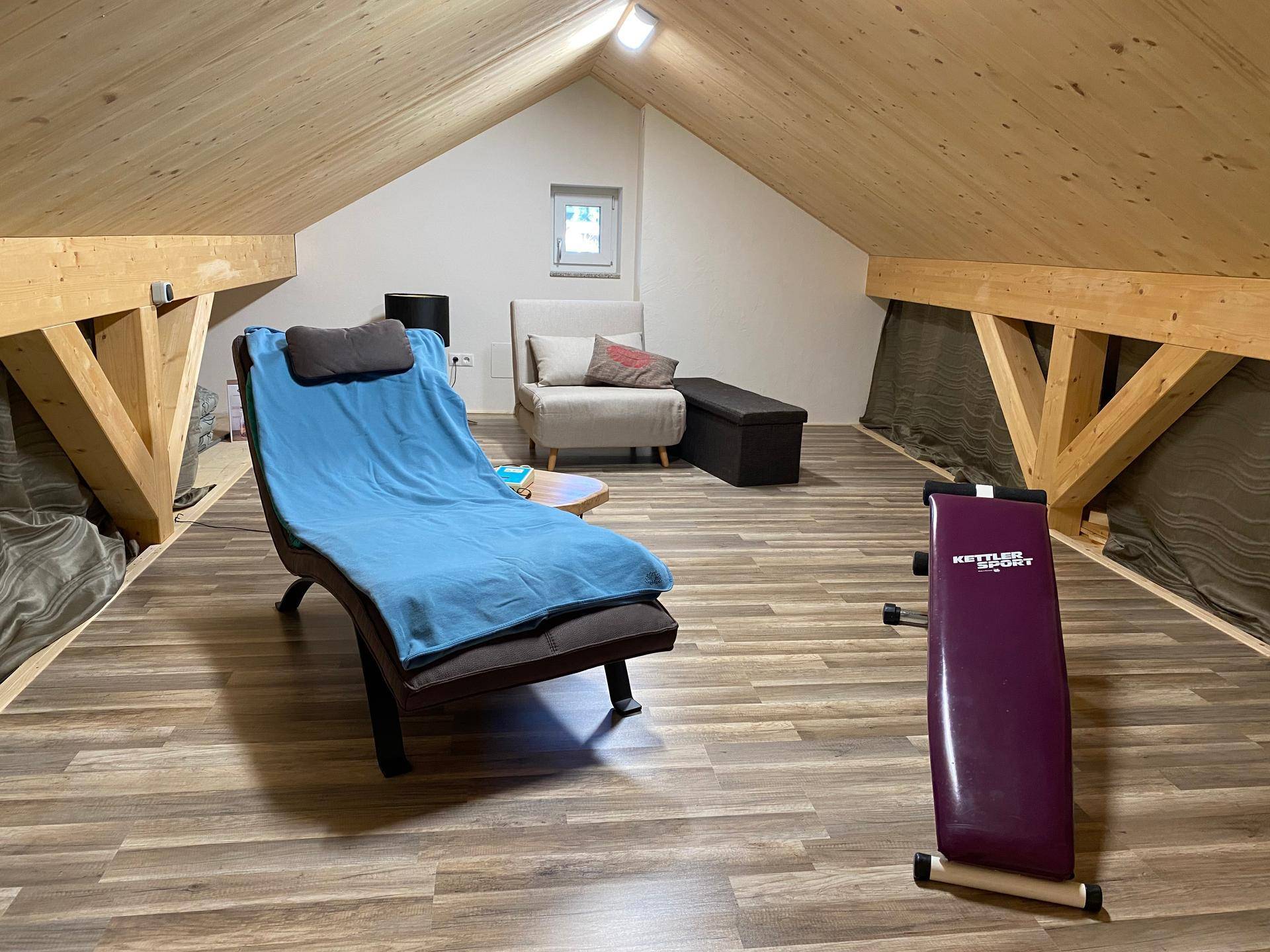 Gemütlicher Dachbodenbereich mit Liegestuhl und Fitnessbank unter der Holzdecke.