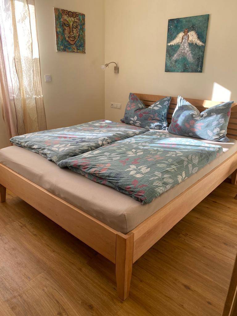 Schlafzimmer mit Doppelbett, Holzboden und farbenfroher Bettwäsche unter natürlichem Licht.