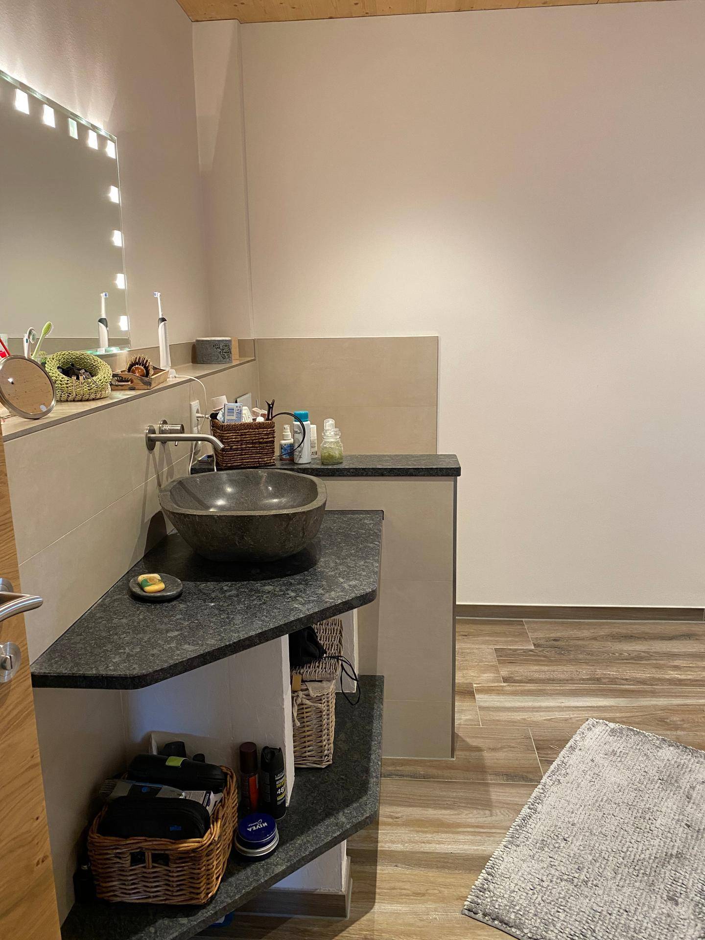Modernes Badezimmer mit Steinwaschbecken, beleuchtetem Spiegel und stilvollen Armaturen.