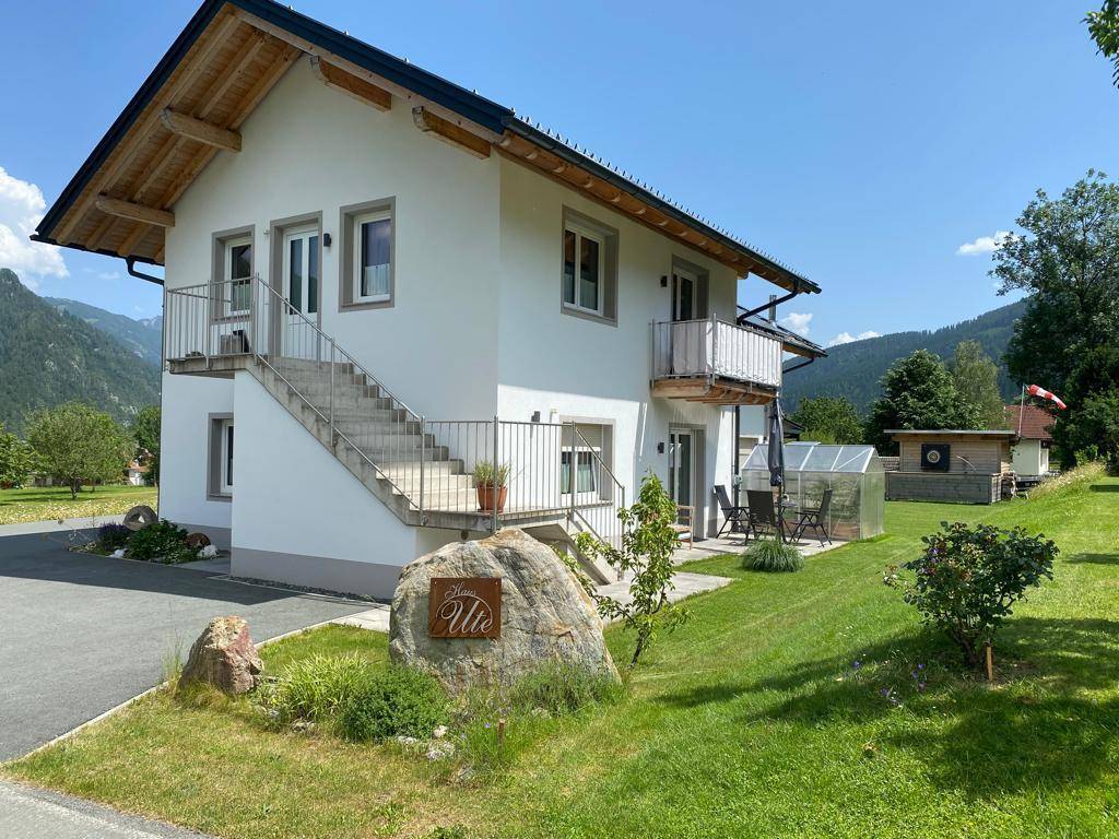 Seitliche Ansicht des Hauses mit Außentreppe, Balkon und einem großen Felsen im Vorgarten.