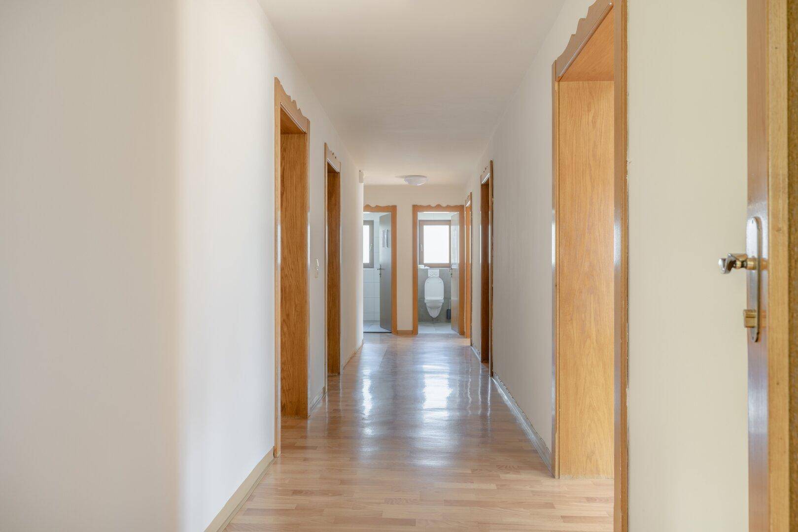 Langer, heller Flur mit Holzboden und mehreren Holztüren, der zu weiteren Räumen führt.