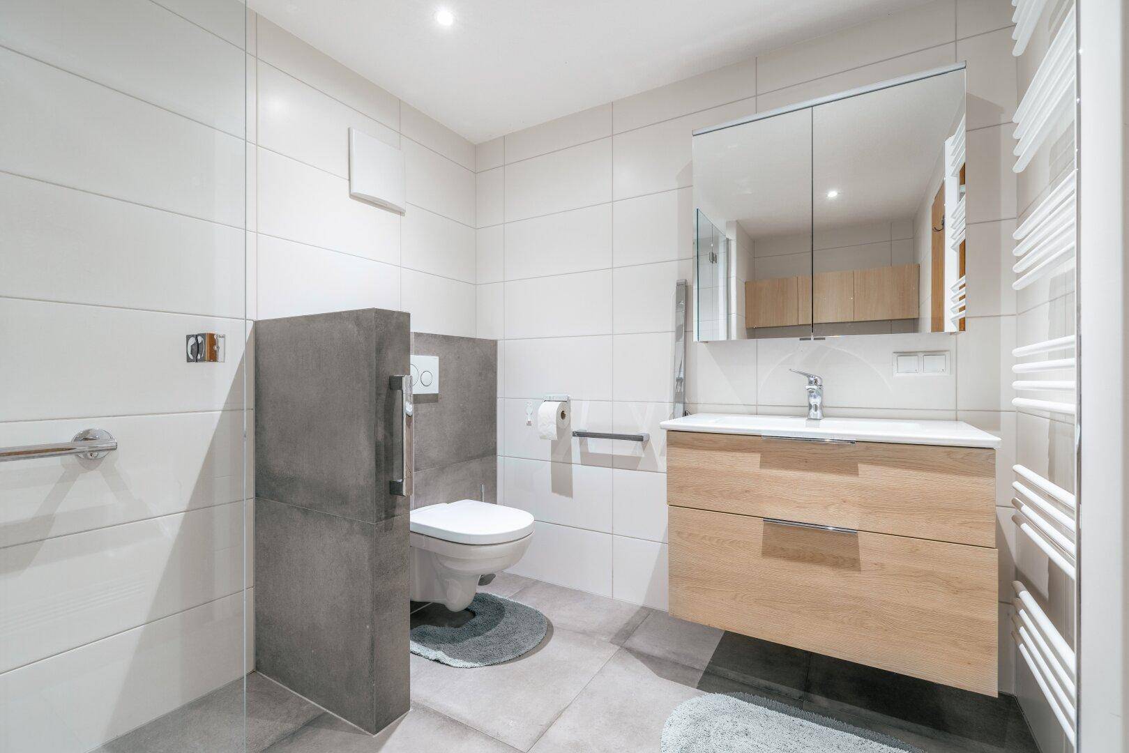 Modernes Badezimmer mit großen weißen Fliesen, schwebendem Waschtisch und Wand-WC.