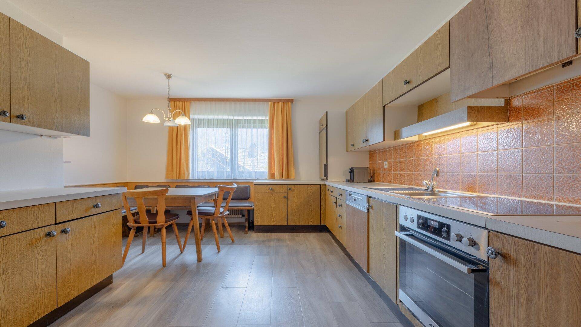 Gemütliche Küche mit Essbereich, Holzschränken, Laminatboden und Fensterblick.