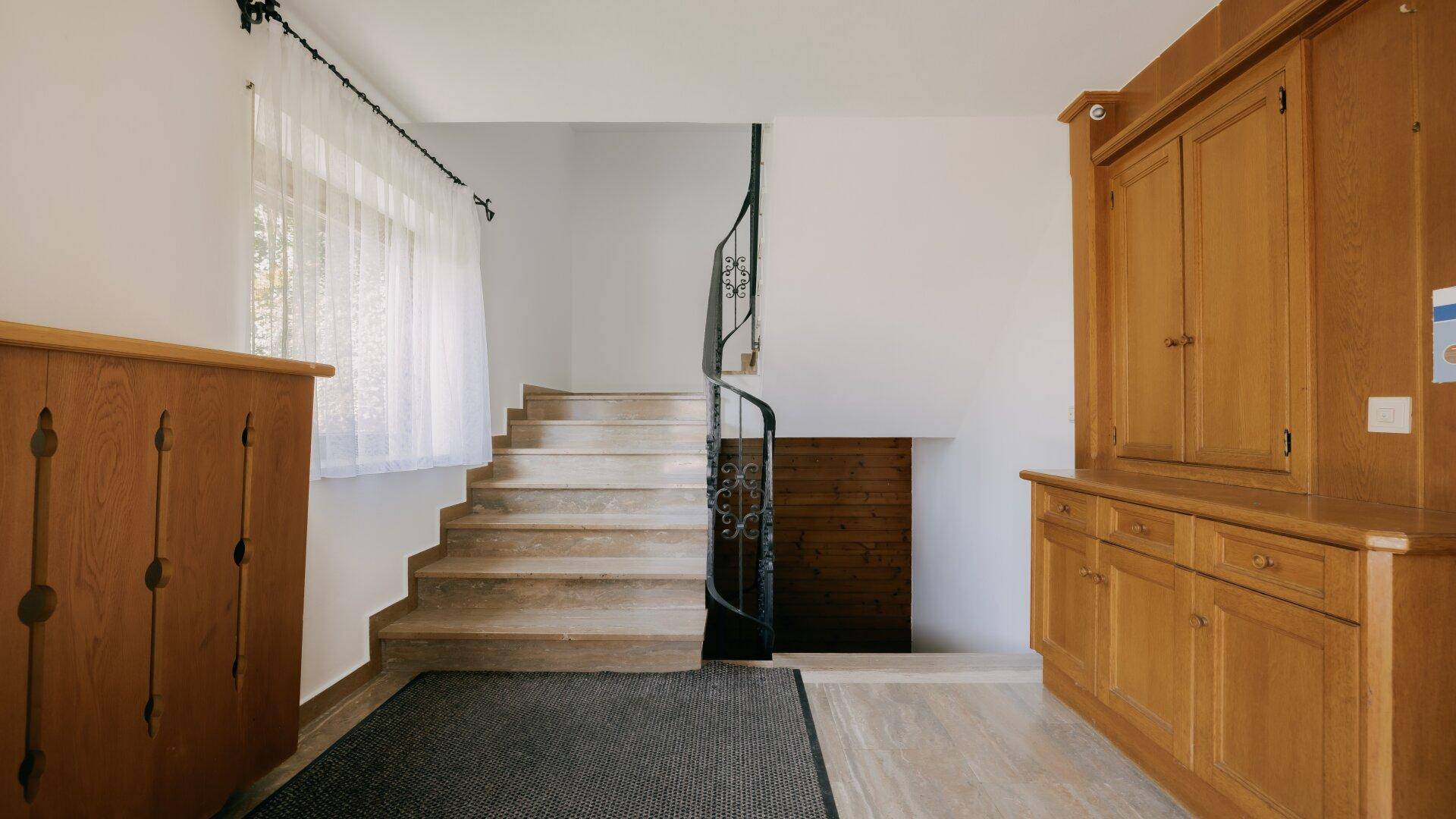 Eingangsbereich mit Holztreppe, schmiedeeisernem Geländer und traditionellen Holzmöbeln.
