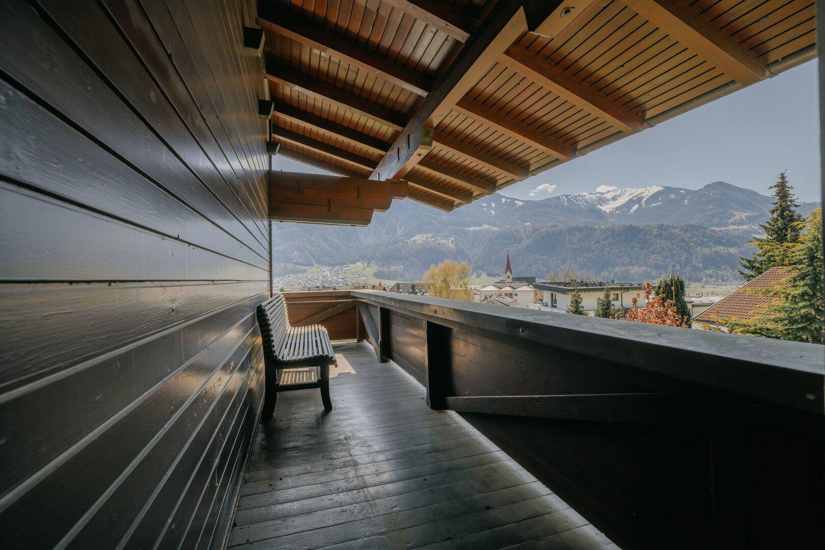 Überdachter Balkon mit Holzboden, Sitzbank und weitem Panoramablick auf die Berge.