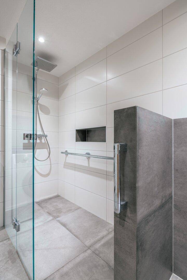 Moderne Duschkabine mit Glaswänden, Regendusche und integrierter Nische für Badutensilien.