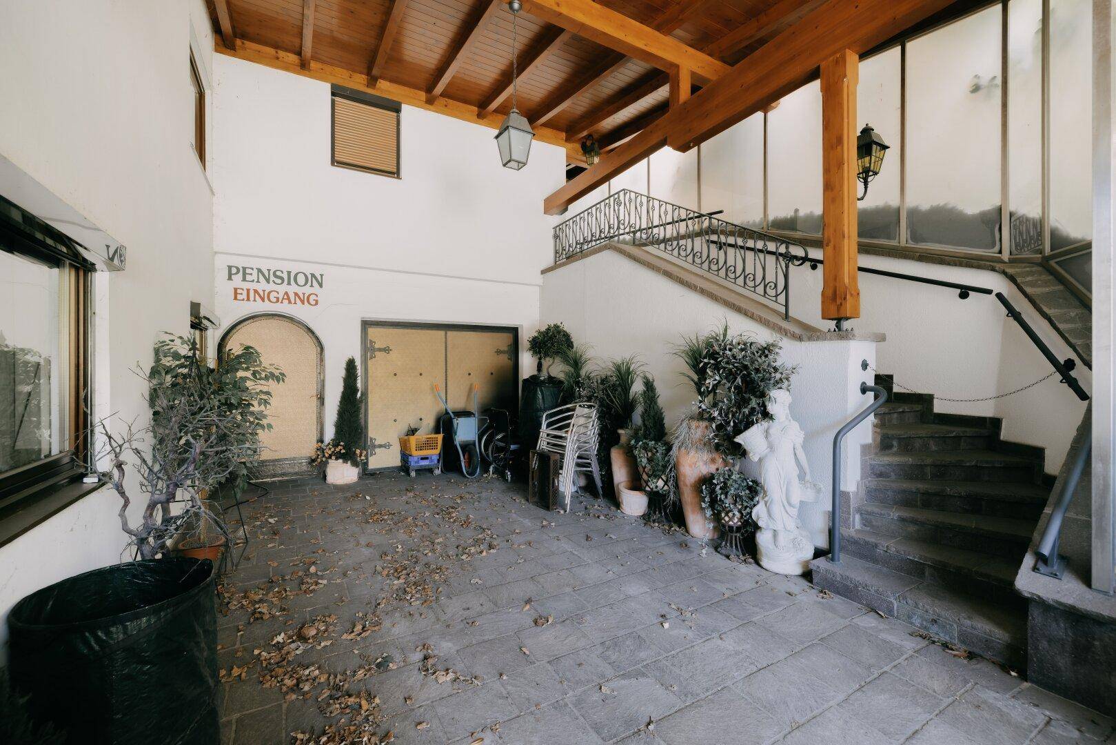 Außenbereich einer Pension mit Steintreppe, Pflanzen und rustikalen Dekorationselementen.