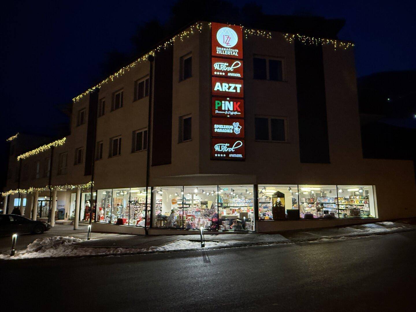 Geschäftsgebäude bei Nacht mit festlicher Weihnachtsbeleuchtung und beleuchteten Schaufenstern.