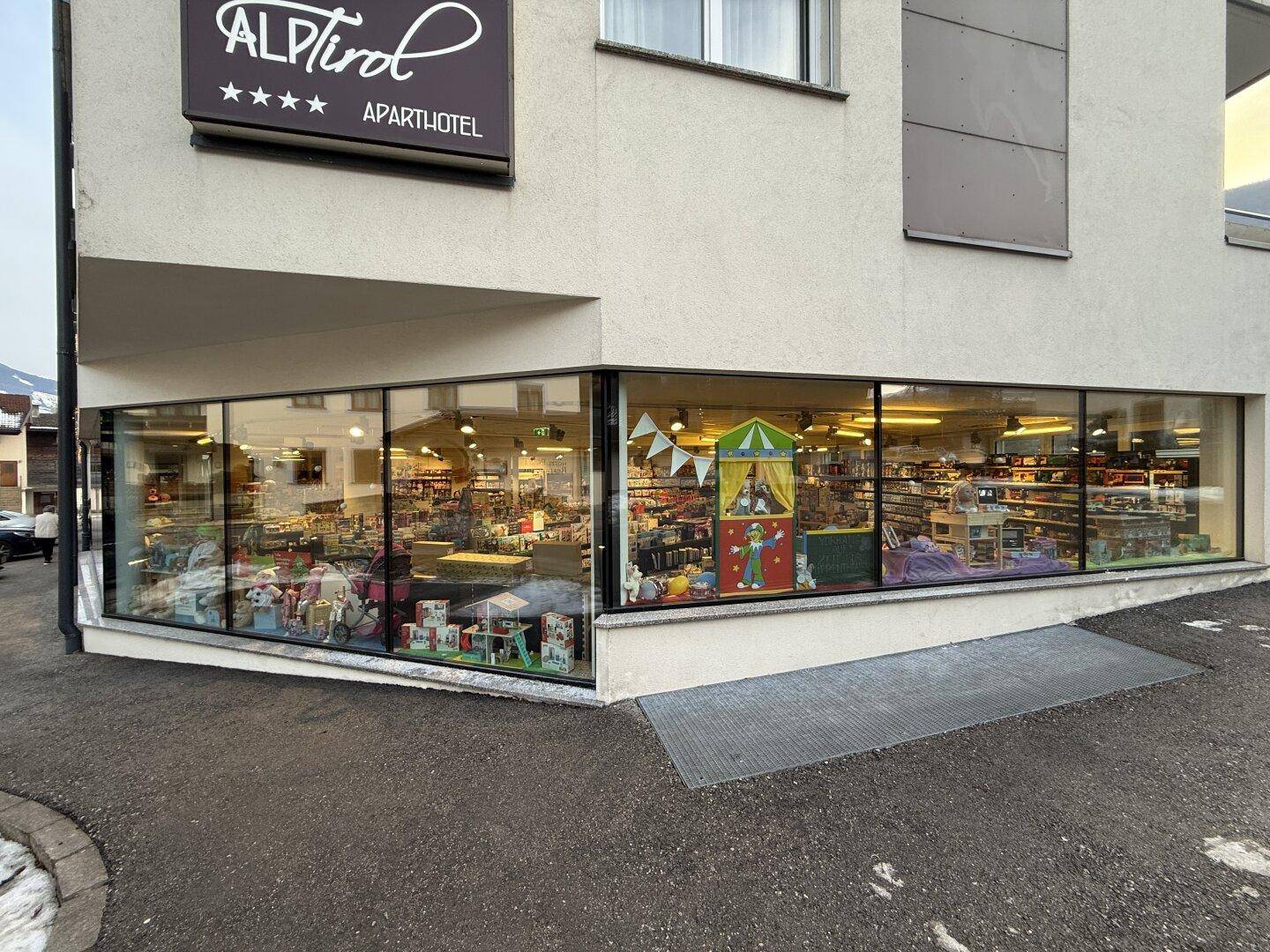 Große Schaufensterfront des Geschäftsgebäudes mit Einblicken in das beleuchtete Ladeninnere.