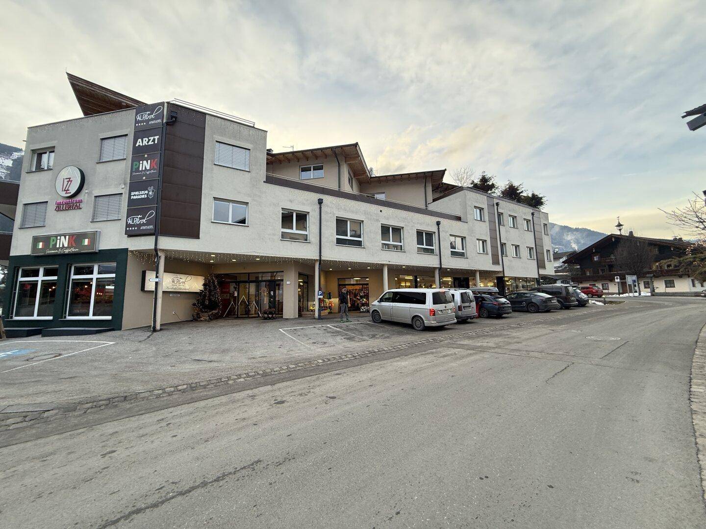 Gesamtansicht des modernen Geschäftsgebäudes mit angrenzender Straße und geparkten Fahrzeugen.