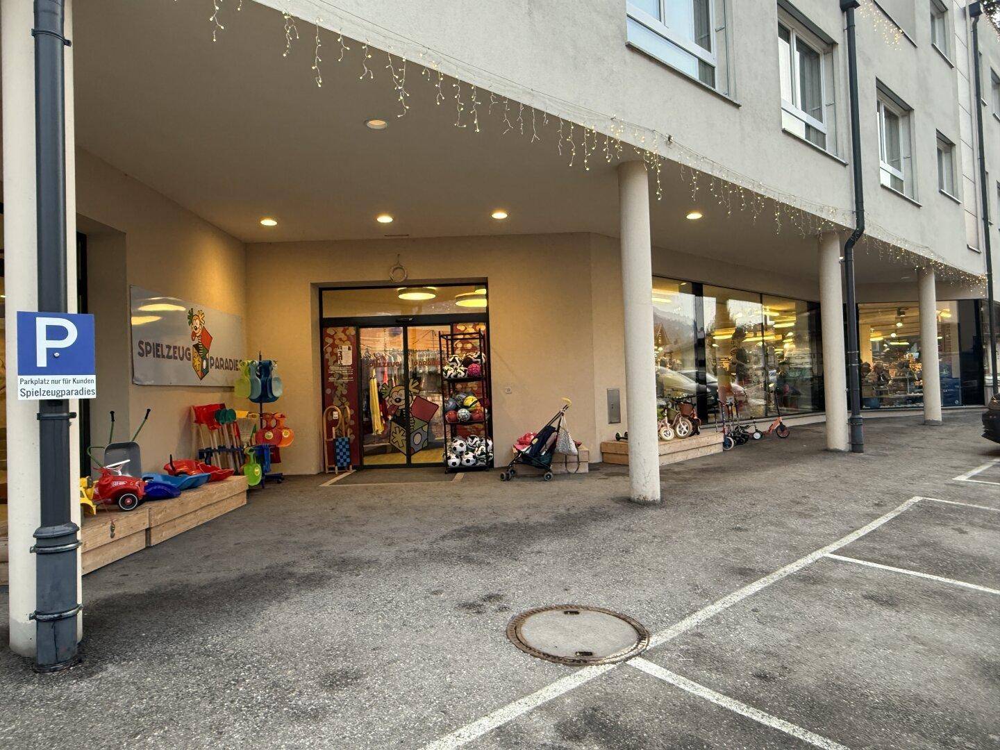 Eingangsbereich des Geschäfts mit Schaufenstern und einem Parkplatz für Kunden.