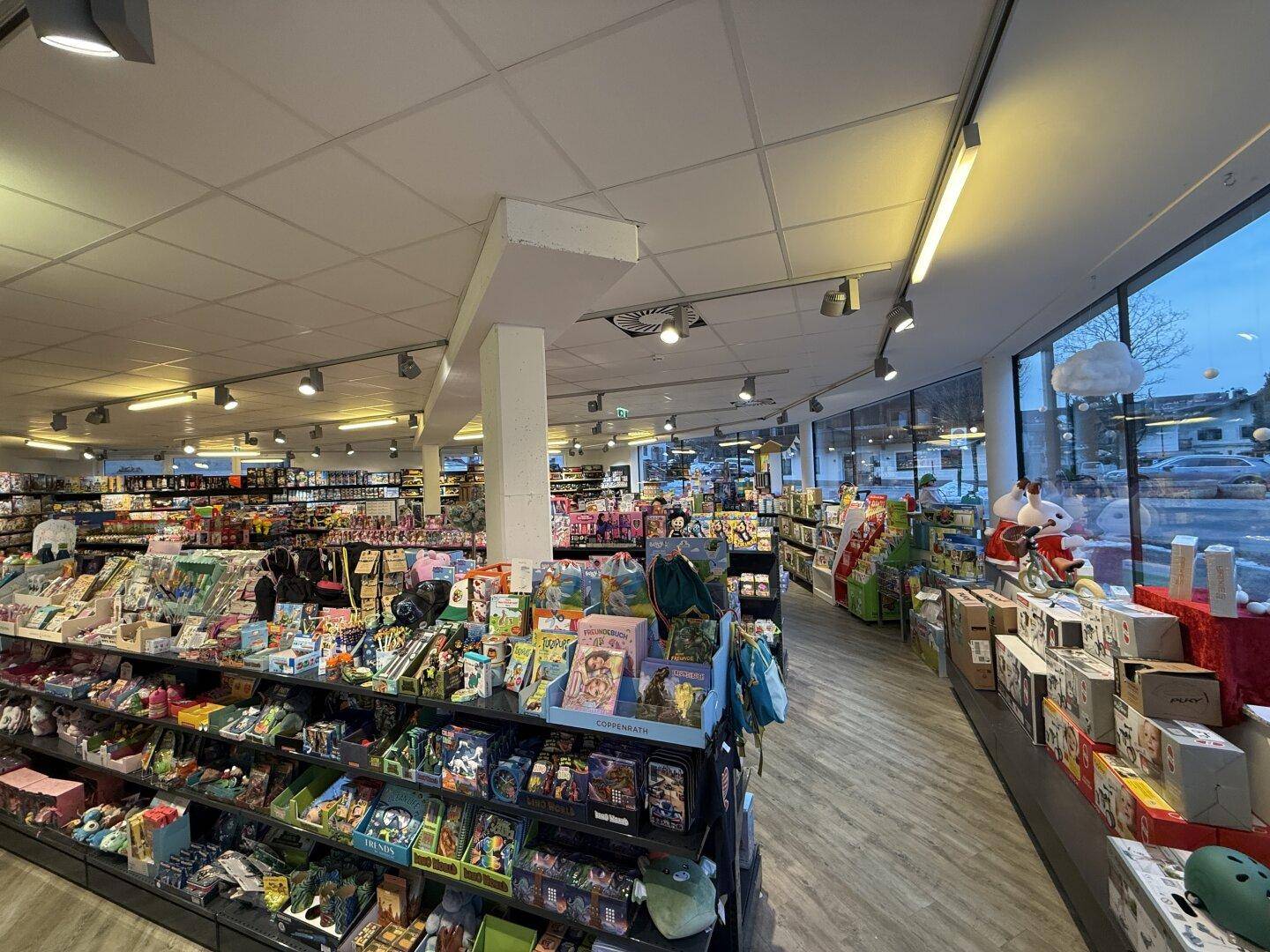 Ladeninneres mit langen Regalen voller Produkte und großen Fenstern zur Straße.