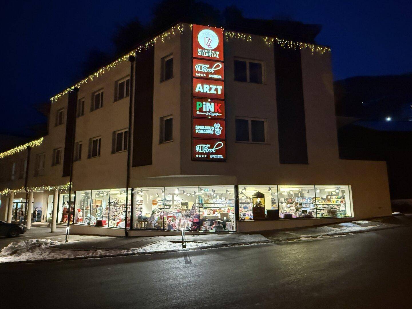 Das Geschäftsgebäude bei Nacht, festlich beleuchtet mit Lichterketten und beleuchteten Ladenfronten.