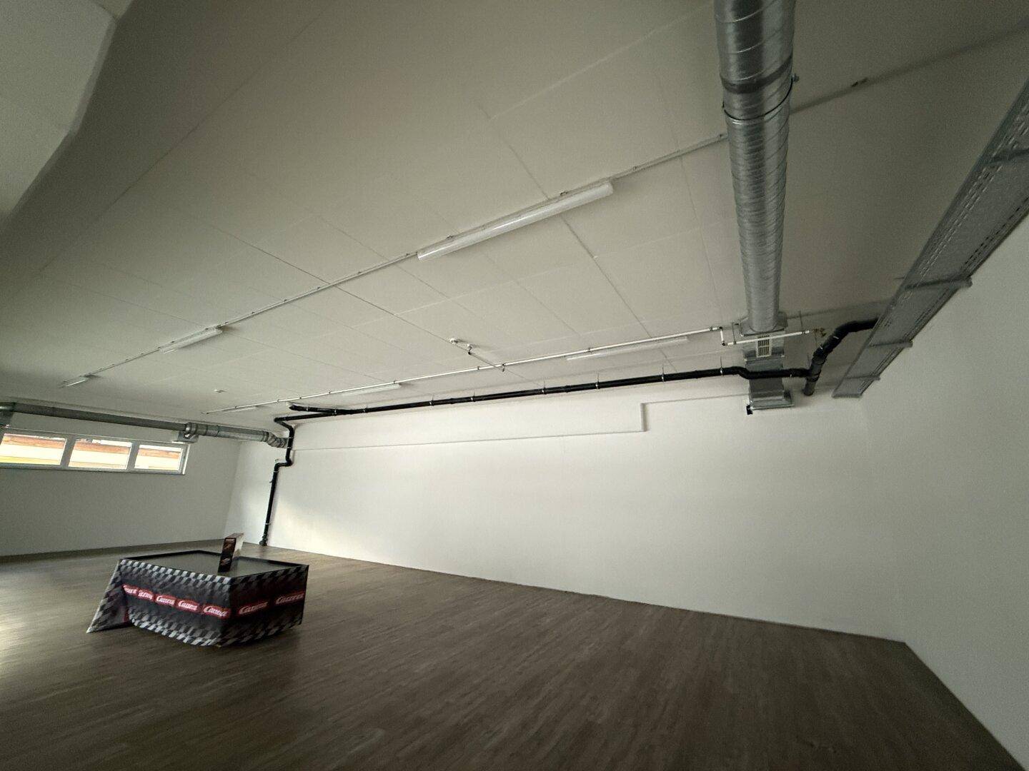 Geräumiger Innenraum mit sichtbaren Lüftungsrohren und Kabelkanälen an der Decke und Wänden.
